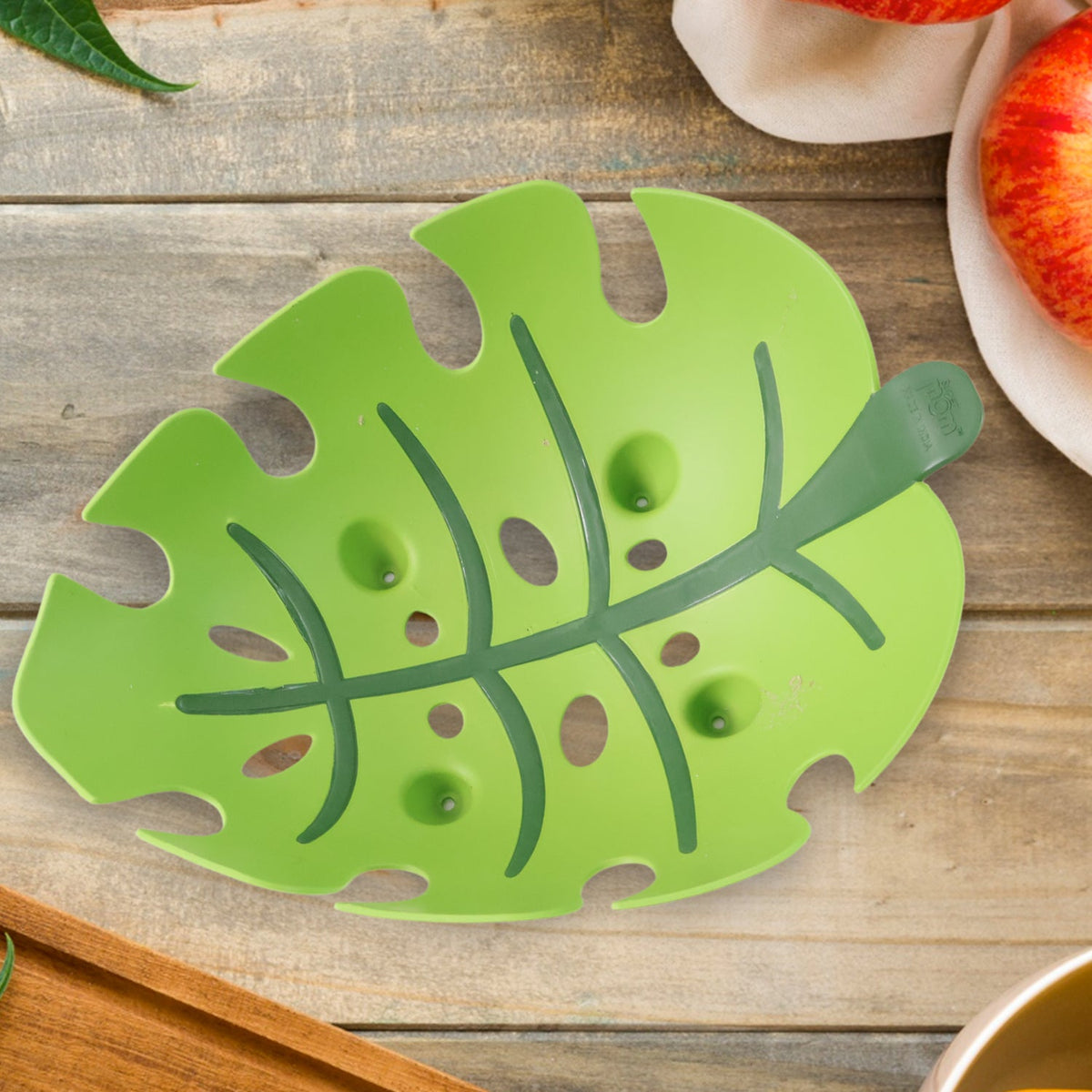 A green leaf-shaped plastic fruit basket with dark green veins lying flat on a rustic wooden table.