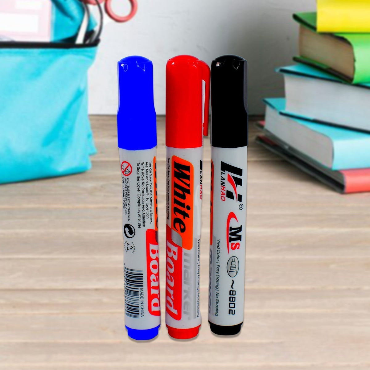 Three whiteboard markers in blue, red, and black standing upright on a wooden surface with blurred books in the background.