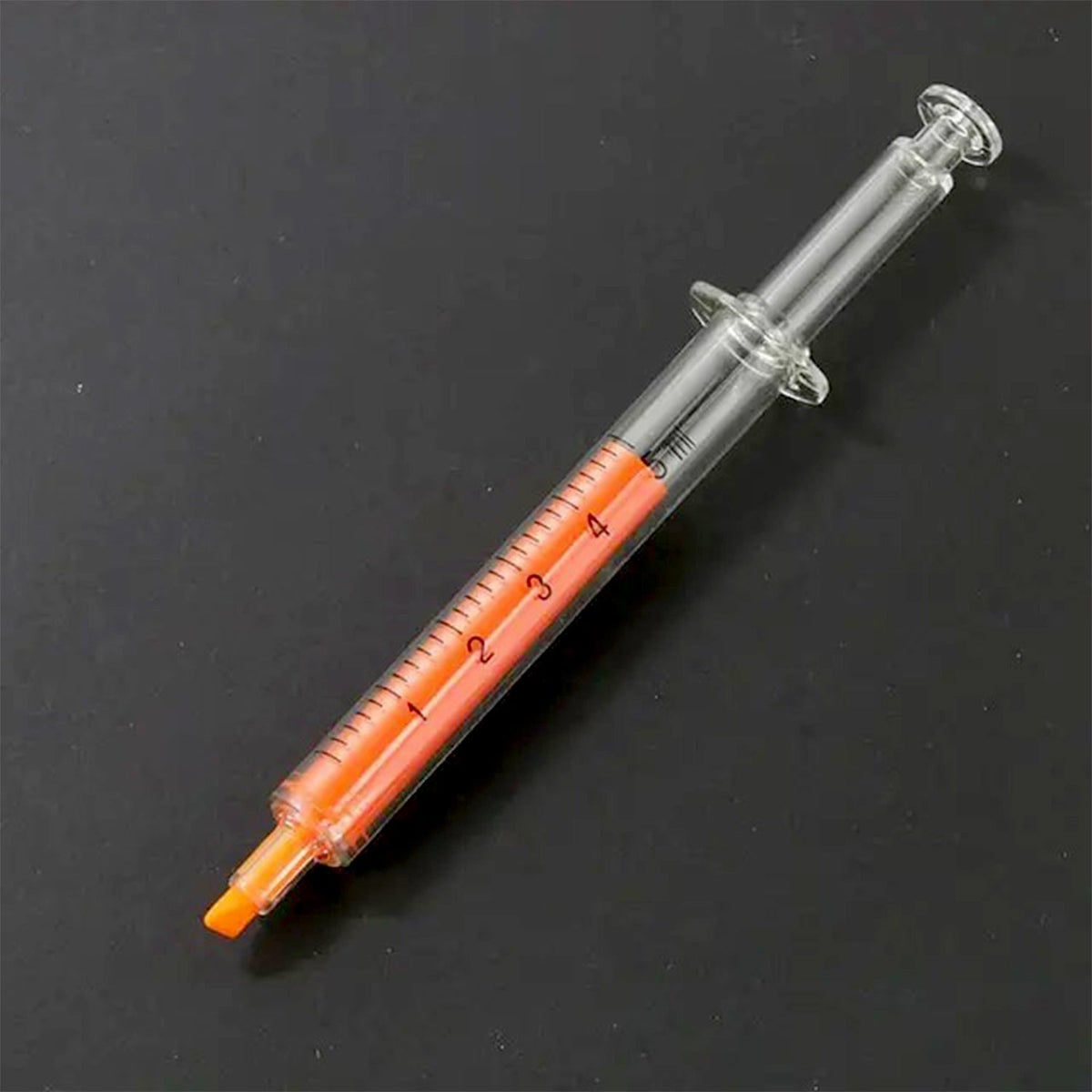A single orange syringe highlighter with a clear barrel and measurements, lying on a black background.