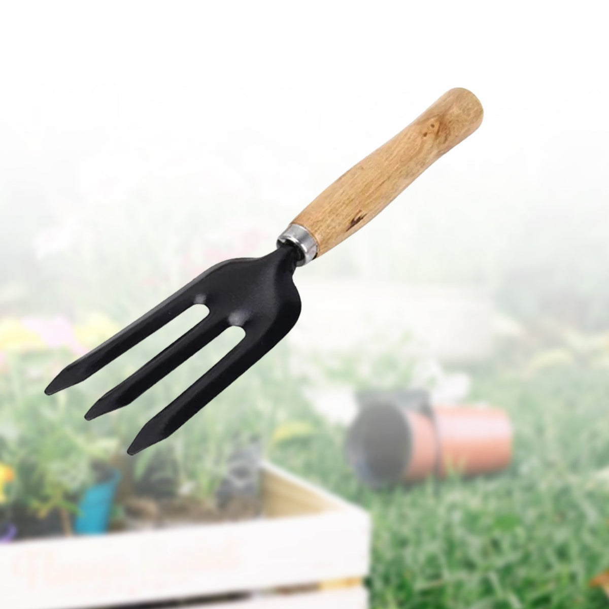 A black three-tine garden fork with a wooden handle is centered against a blurred background of green grass and a white