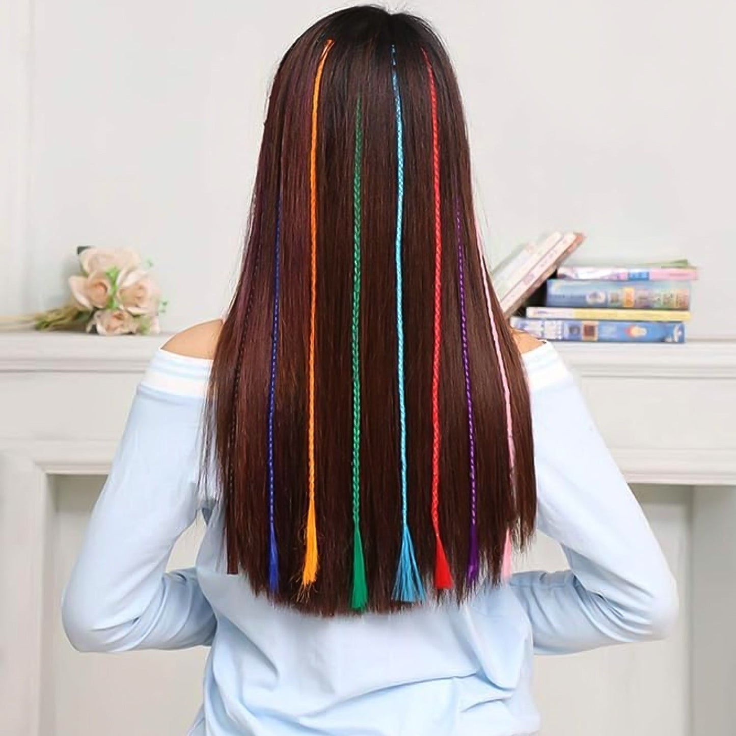 A woman with long brown hair from behind, showing multiple colorful braided hair extensions clipped in.