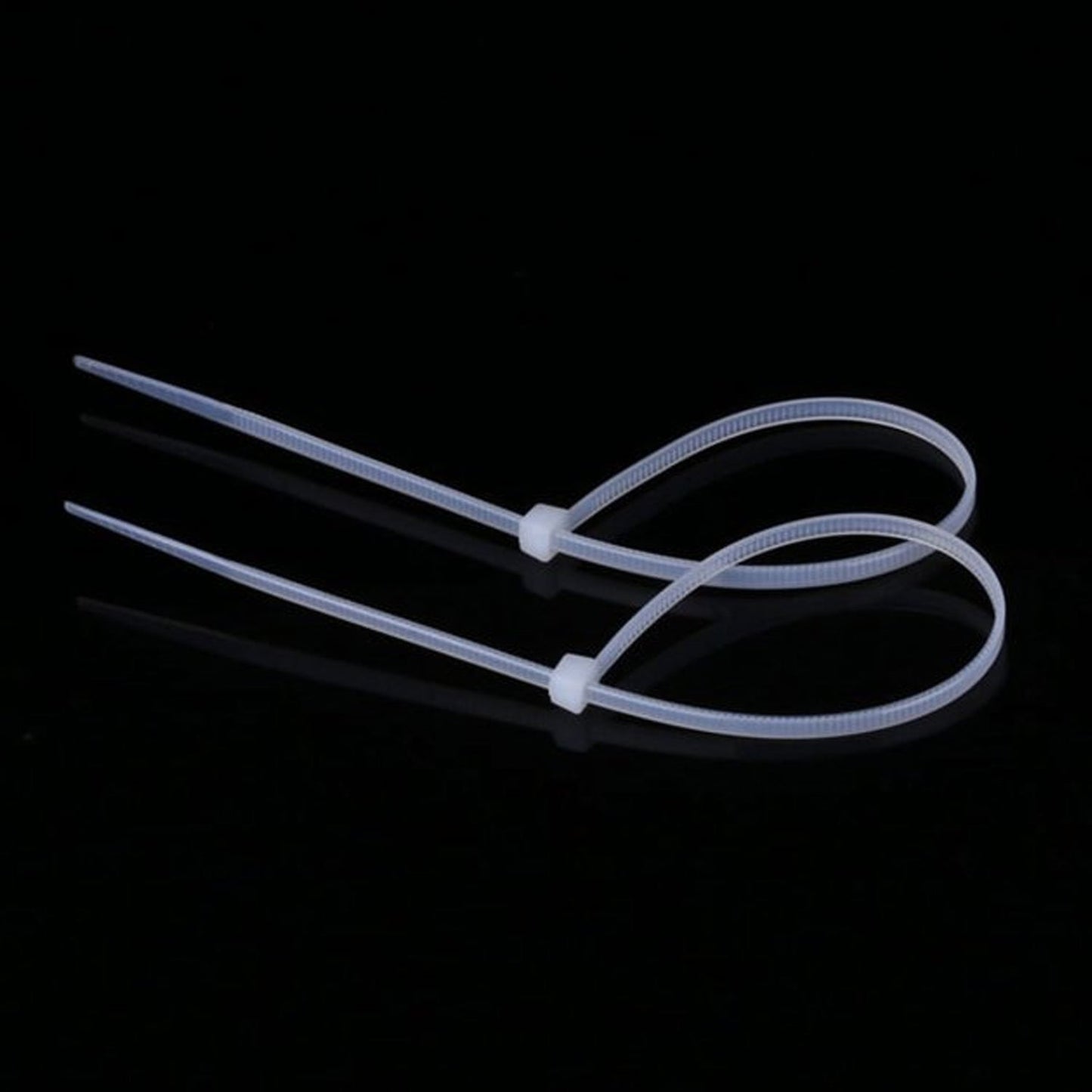 Two white cable ties, looped and secured, lying on a dark, reflective surface.