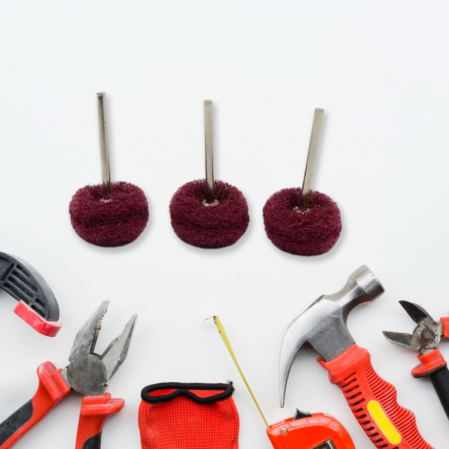 Three maroon buffing wheels surrounded by various hand tools on a white surface.