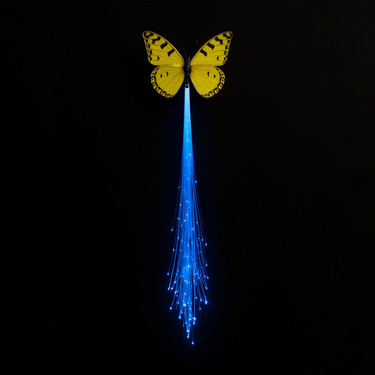A yellow butterfly hair clip with bright blue glowing fiber optic strands hangs vertically against a dark background.