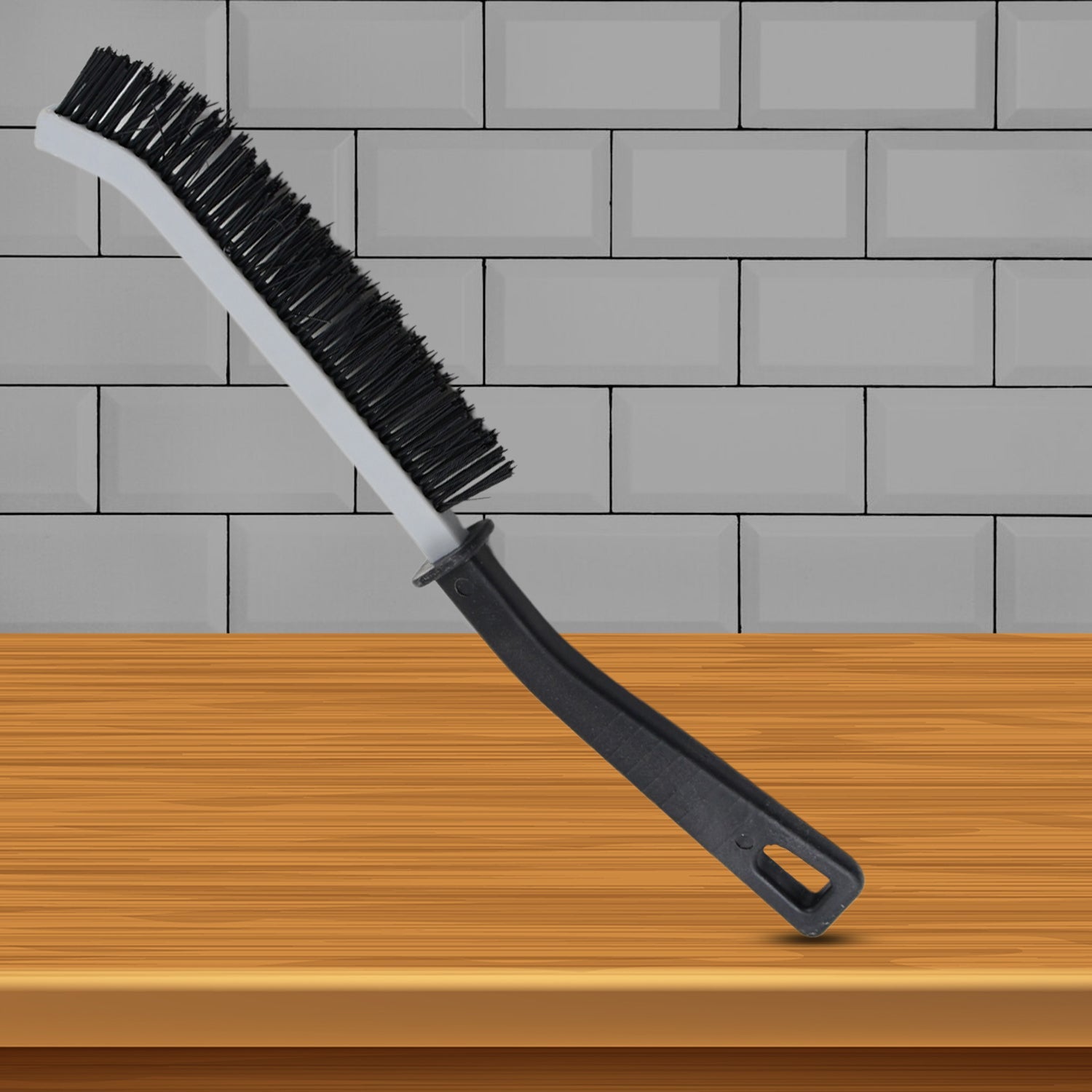 A black and gray crevice cleaning brush stands upright on a wooden surface against a gray tiled wall.
