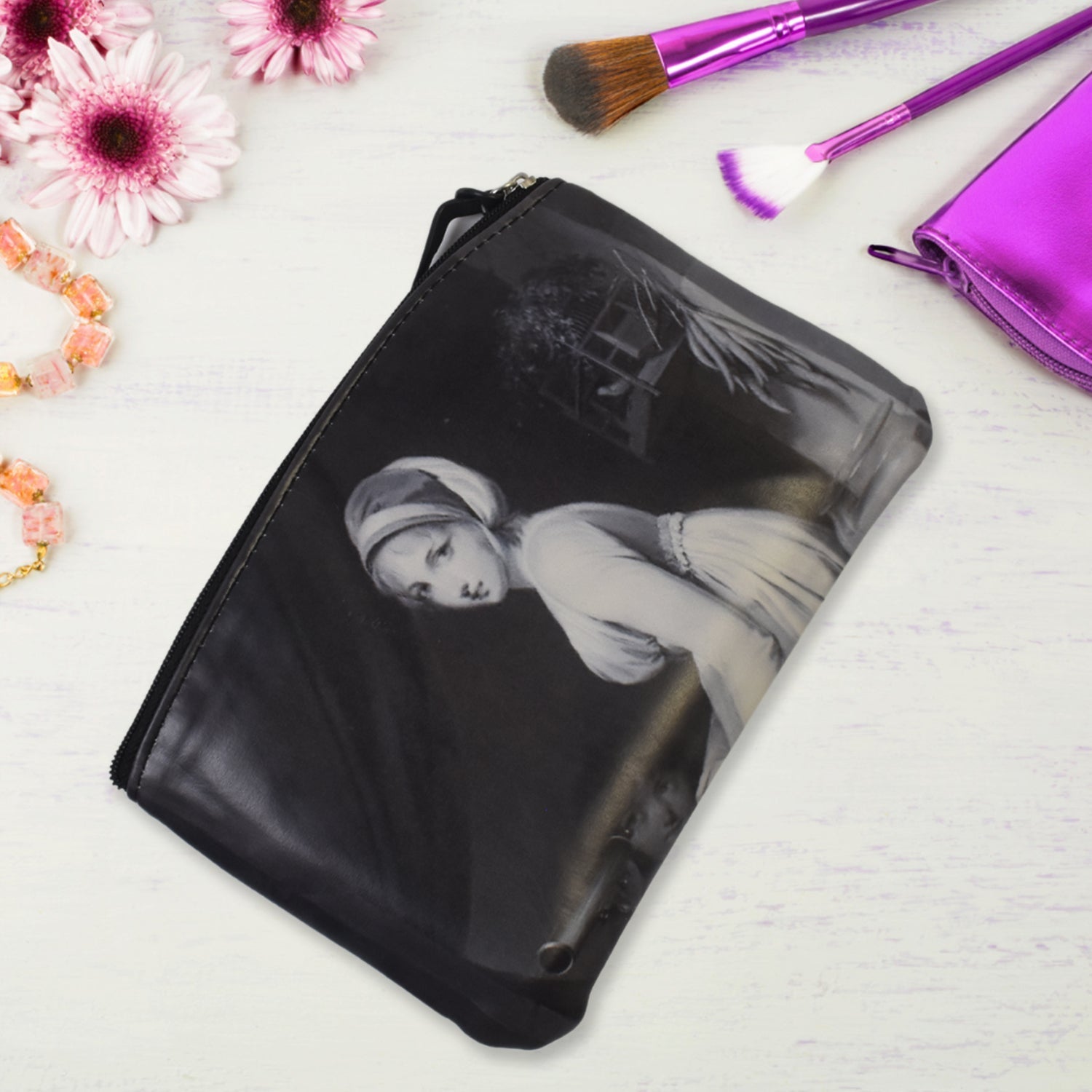 A black travel pouch with a classic painting, surrounded by various makeup products on a white background.