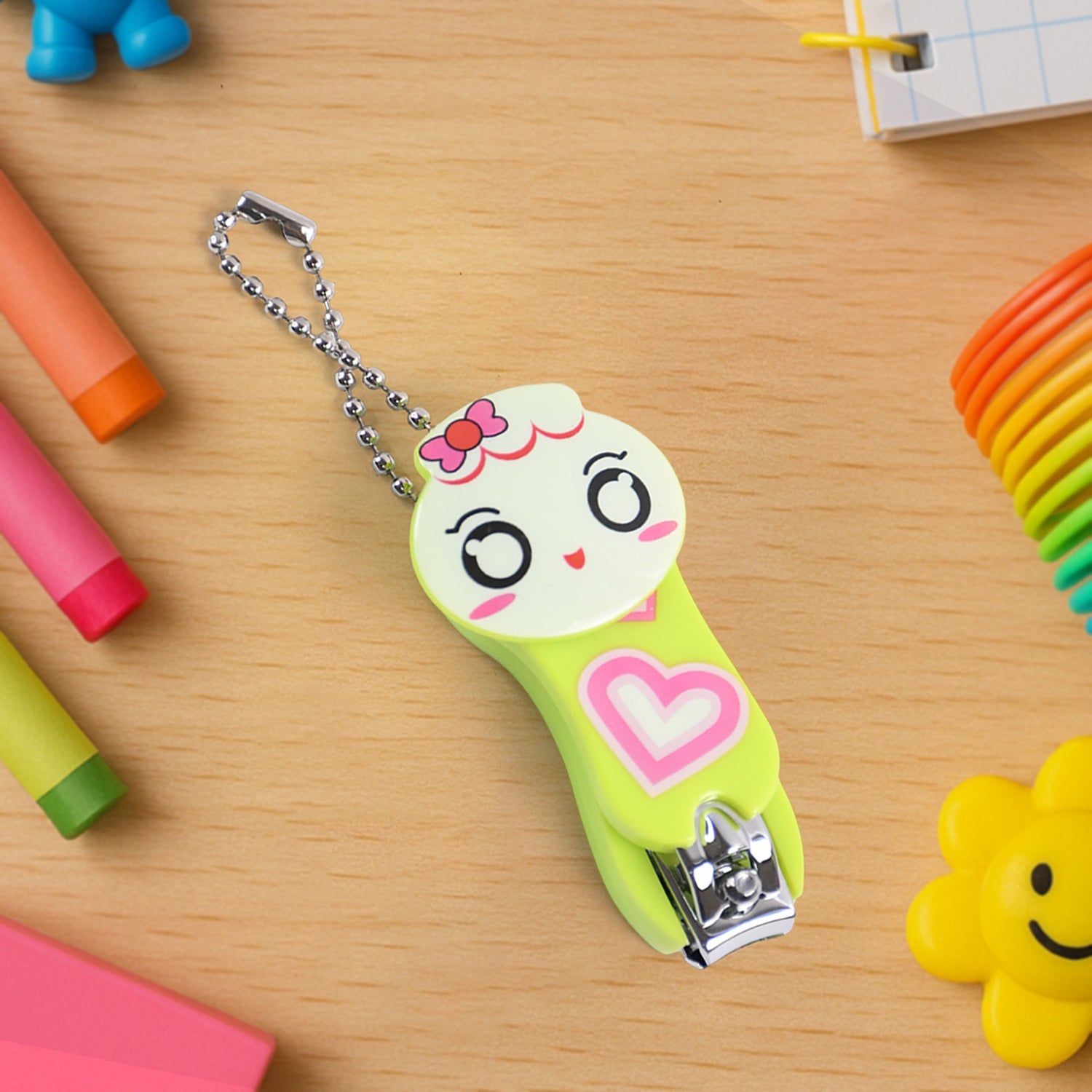 A green and white cartoon character nail clipper with a pink heart and a silver ball chain, surrounded by colorful school