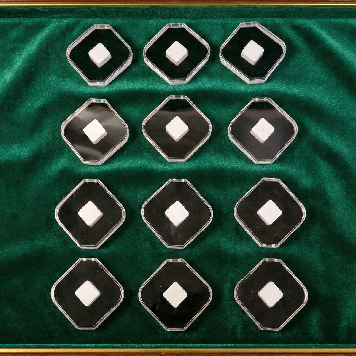 Twelve clear and black jewellery boxes with white cushions, arranged on a green velvet surface