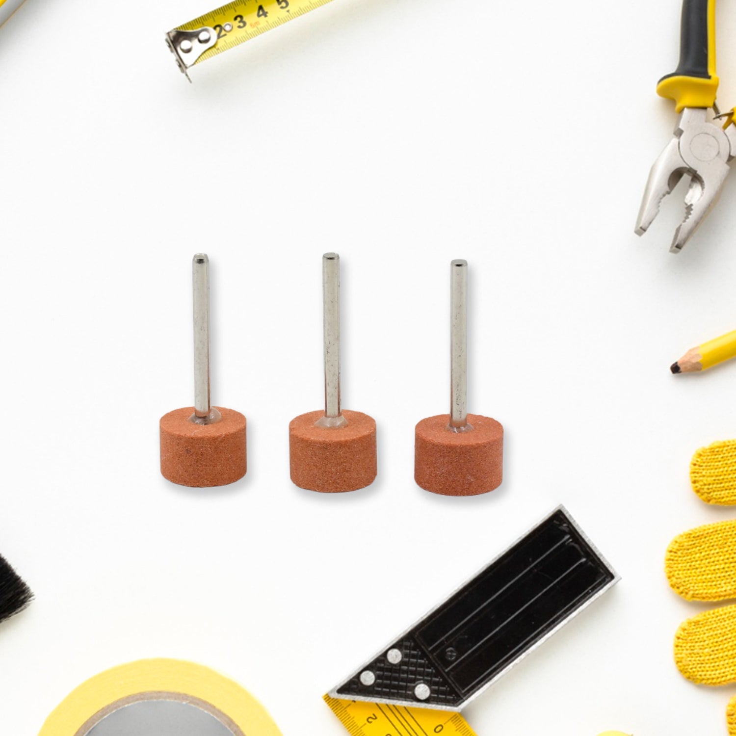 Three cylindrical abrasive grinding wheels in a row on a white surface with various yellow and black tools.