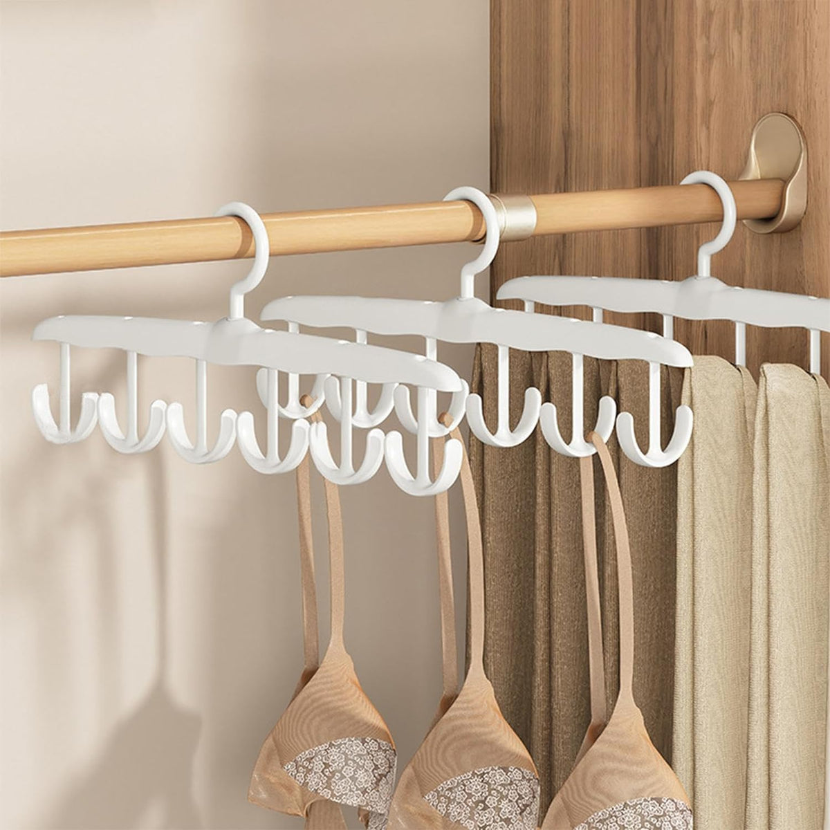 Three white plastic multi-hook hangers on a wooden rod, holding bras and pants in a closet.