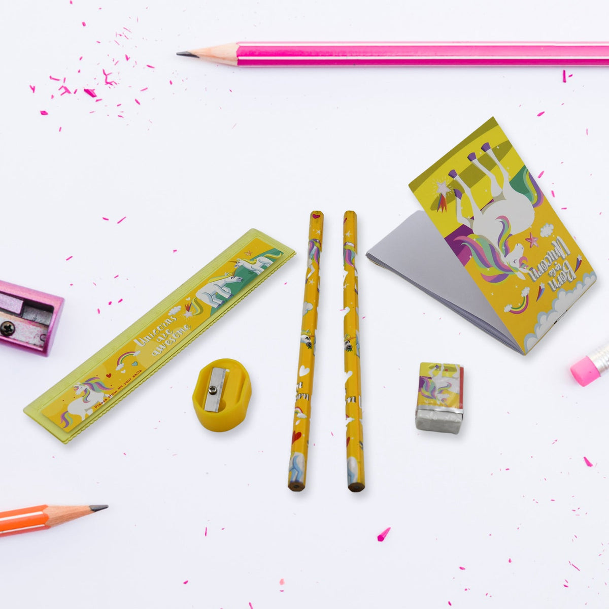 Unicorn-themed pencils, ruler, sharpener, eraser, and notebook on a white surface with pink pencil shavings and a pink