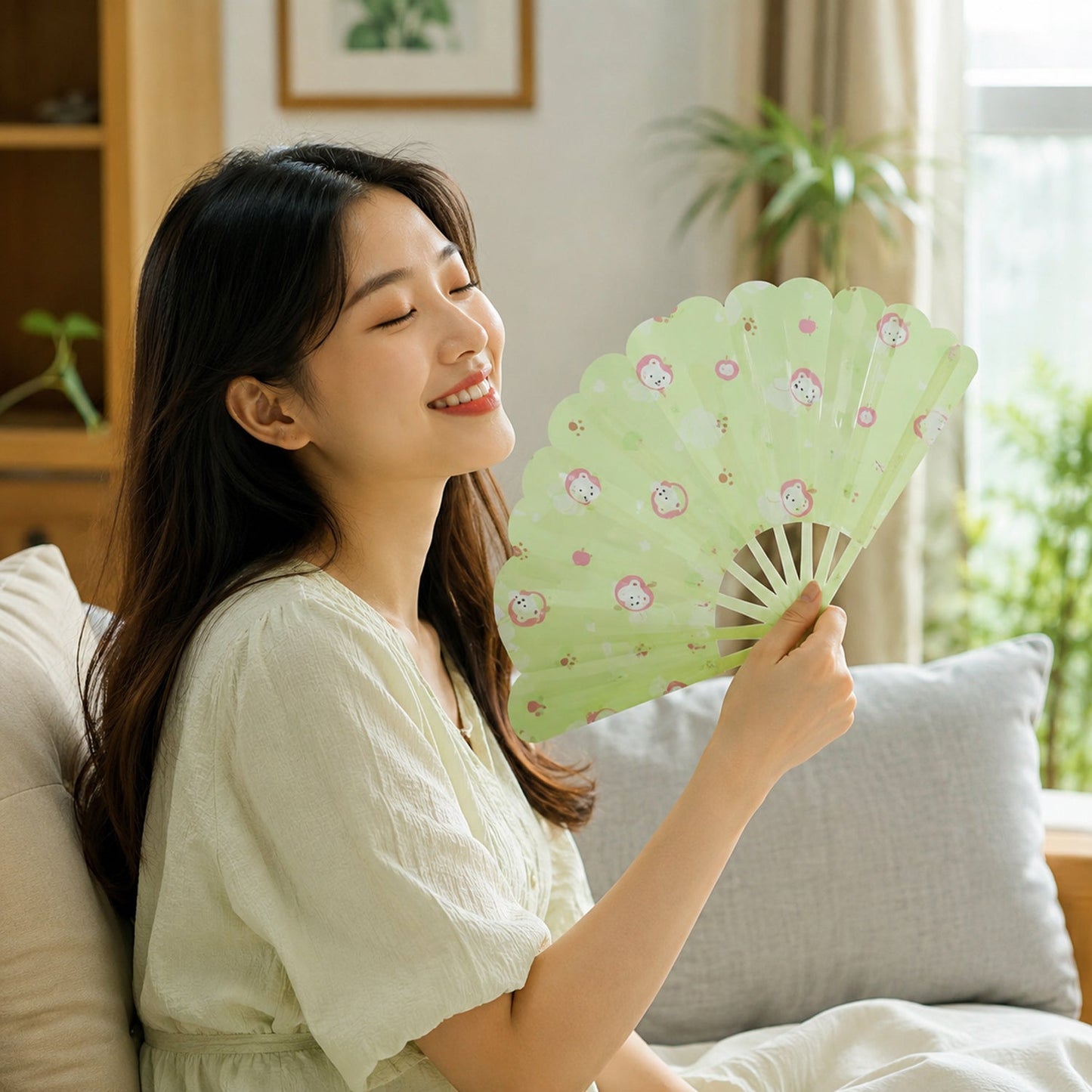 A smiling woman in a light dress sits on a sofa, fanning herself with a green plastic fan.