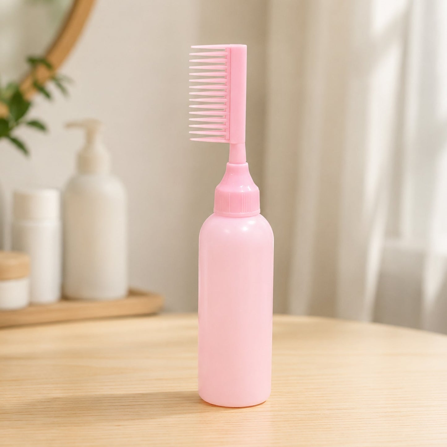 A pink 2 In 1 Hair Oil Applicator Bottle with Scalp Comb stands on a wooden surface with blurred bathroom items behind it.