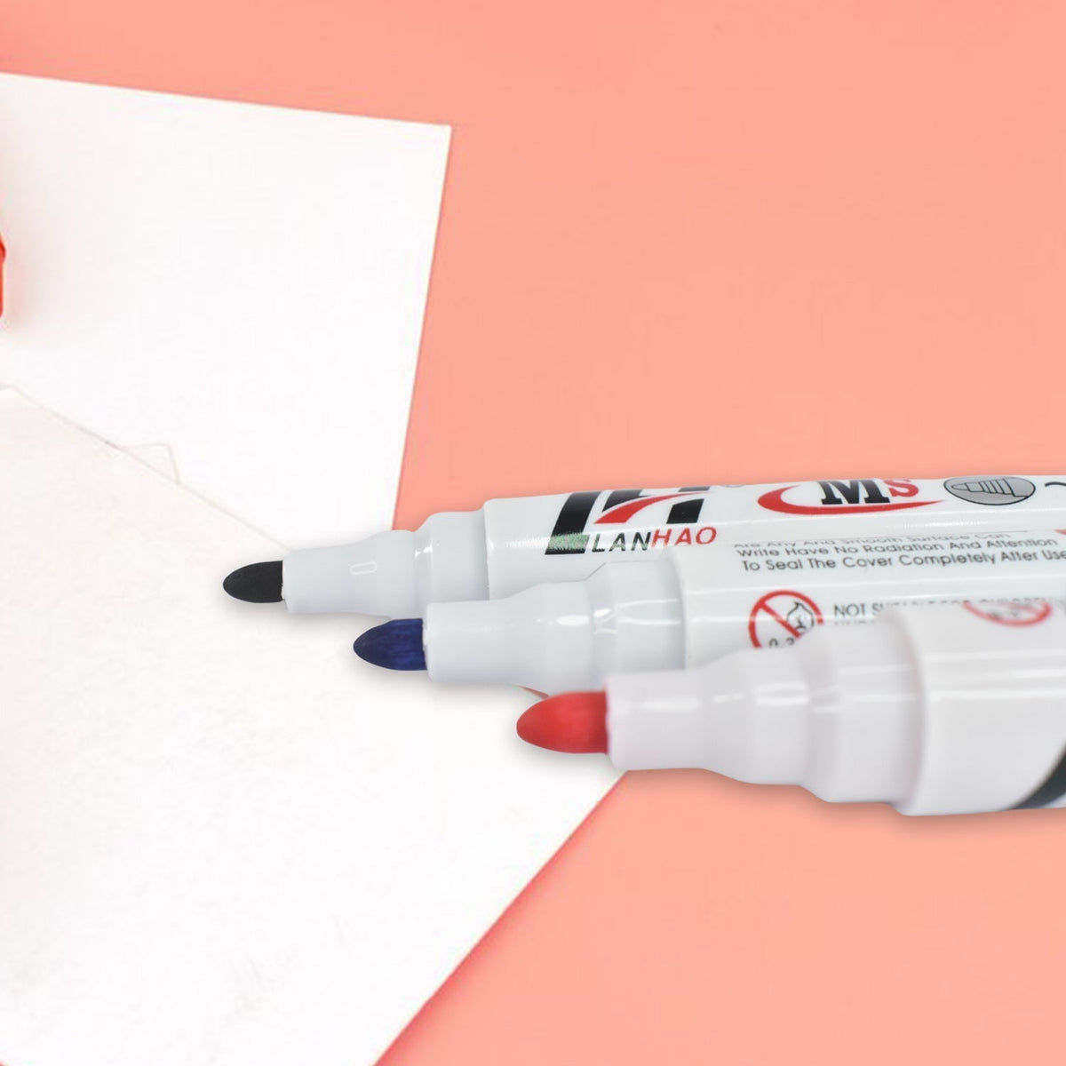 Three whiteboard markers in black, blue, and red, with their tips visible, resting on a white surface with a pink background.