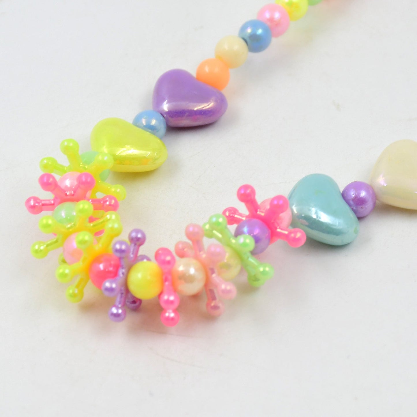 A close-up view of the colorful beaded necklace shows iridescent heart and star-shaped beads in various pastel colors.