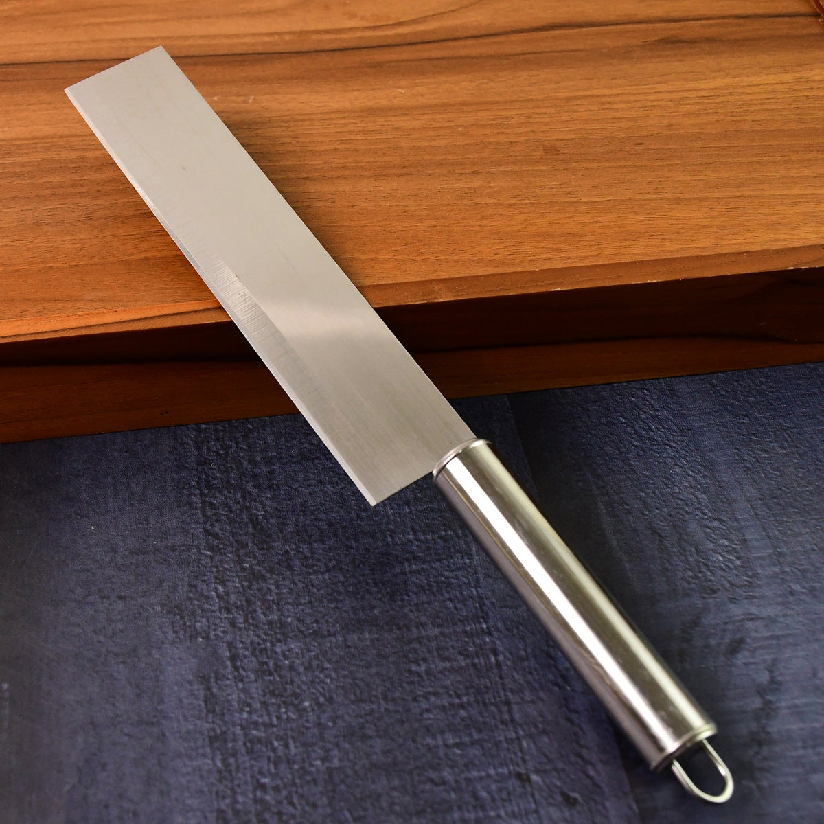A stainless steel cleaver knife with a brushed finish and a silver handle is positioned against a dark and light wood