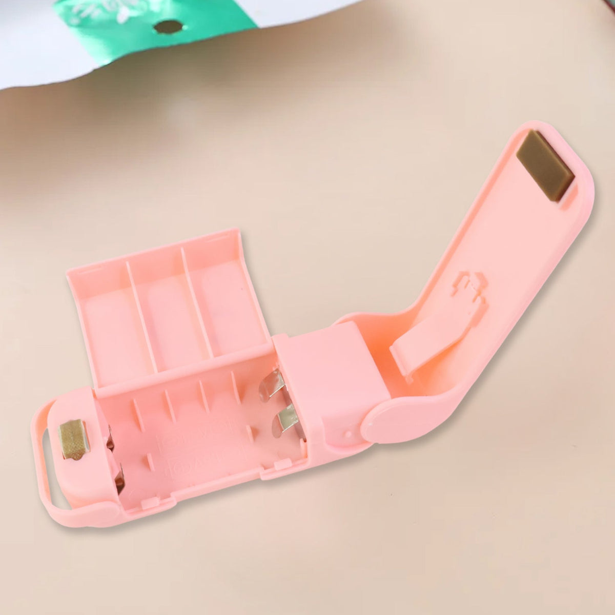 The pink plastic bag sealer is open, revealing the battery compartment and internal mechanisms against a light background.