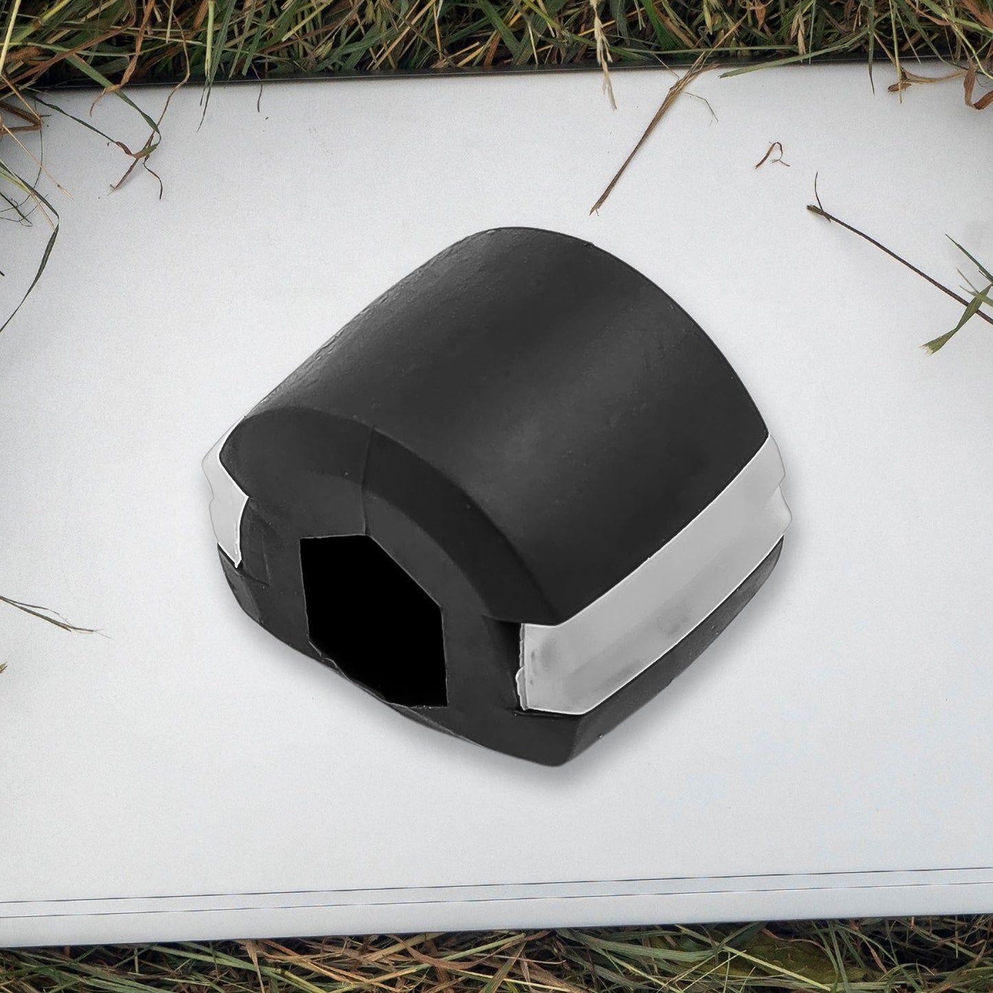 A black and white jaw exerciser rests on a white surface surrounded by green grass and dry twigs.