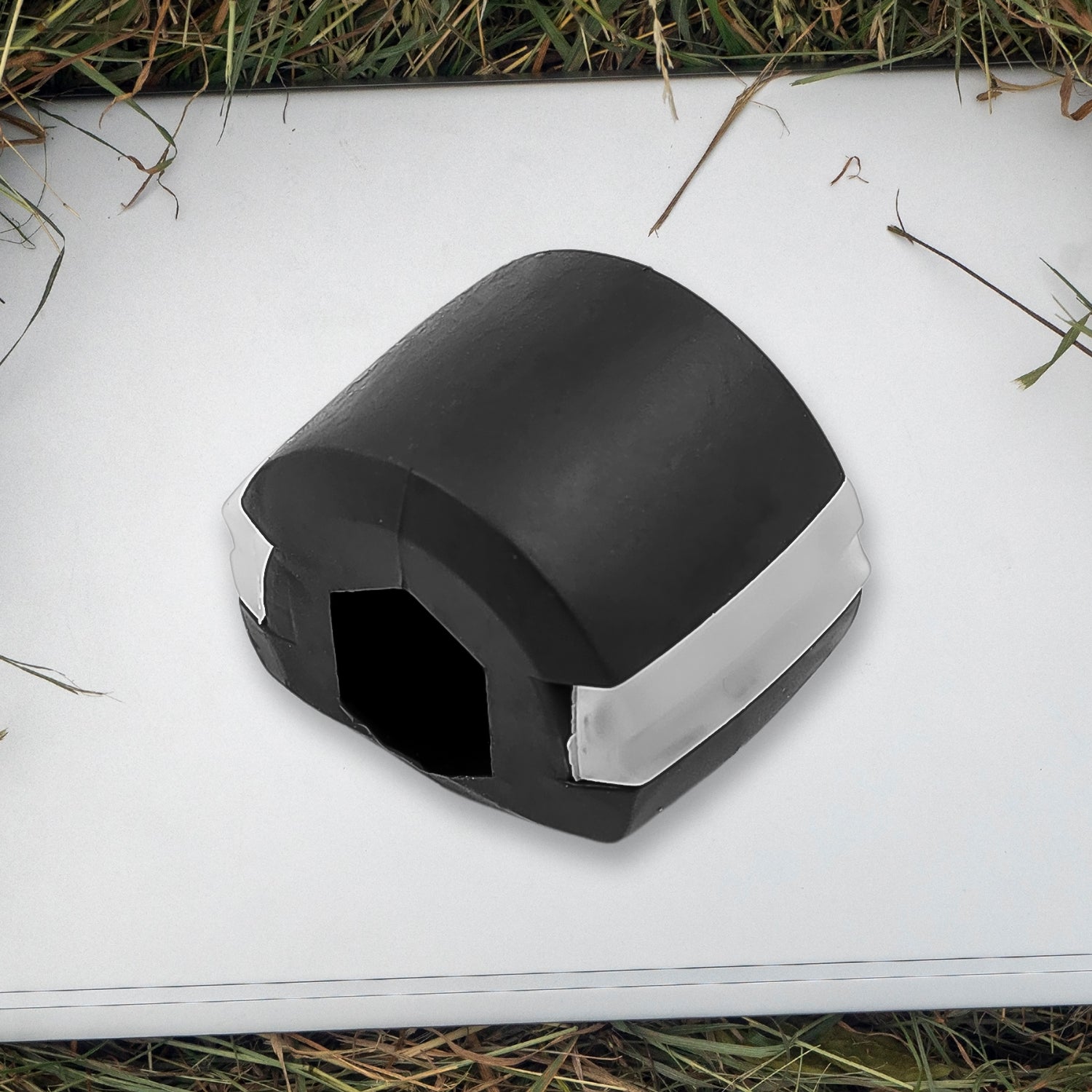 A black and white jaw exerciser rests on a white surface surrounded by green grass and dry twigs.