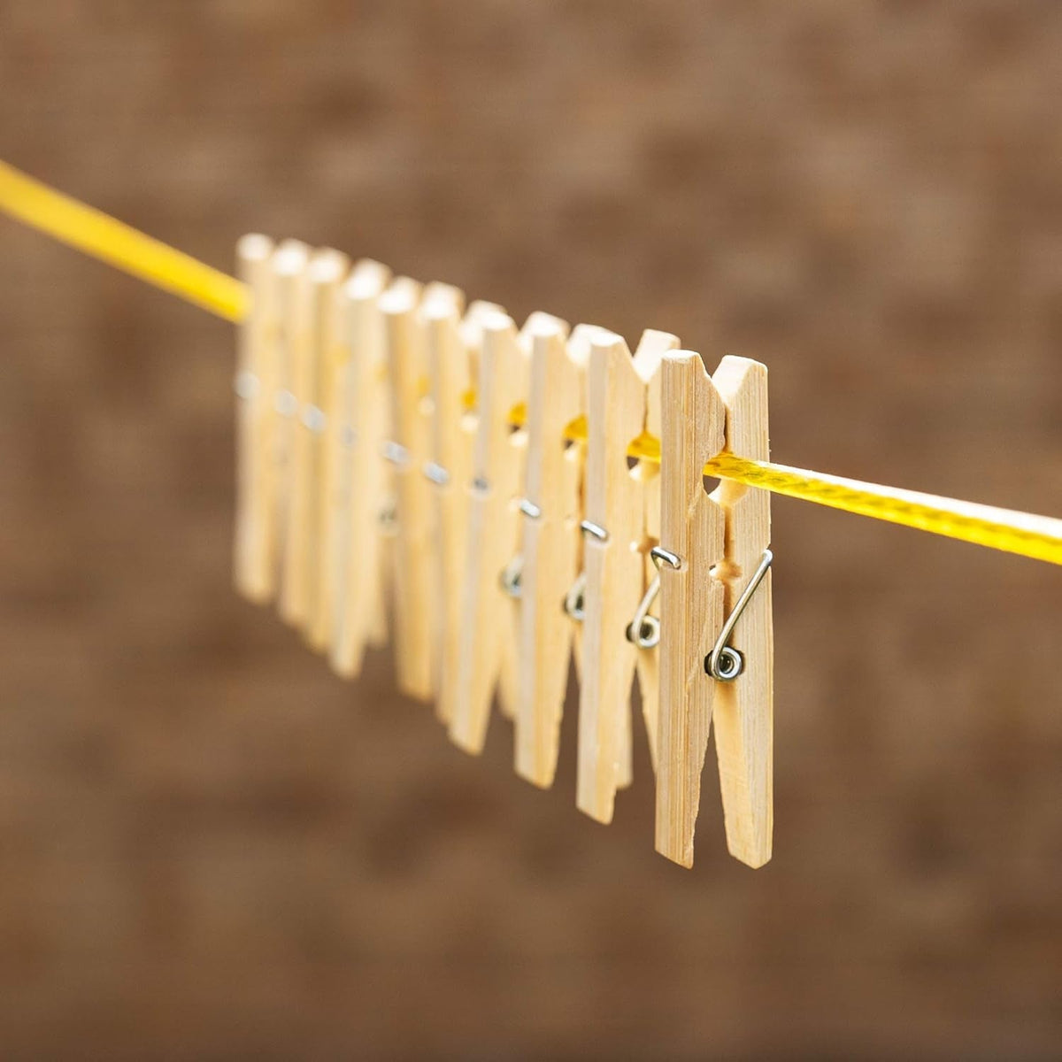 A row of ten natural bamboo clothes pegs clipped onto a yellow clothesline against a blurred brown background.