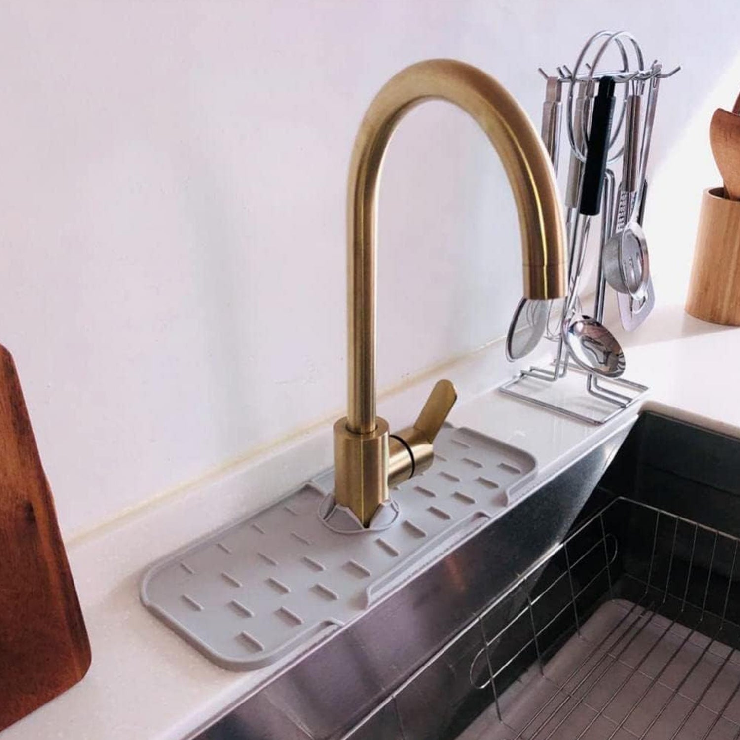 Gray silicone faucet splash guard in a kitchen sink with a gold-colored faucet and utensil holder.
