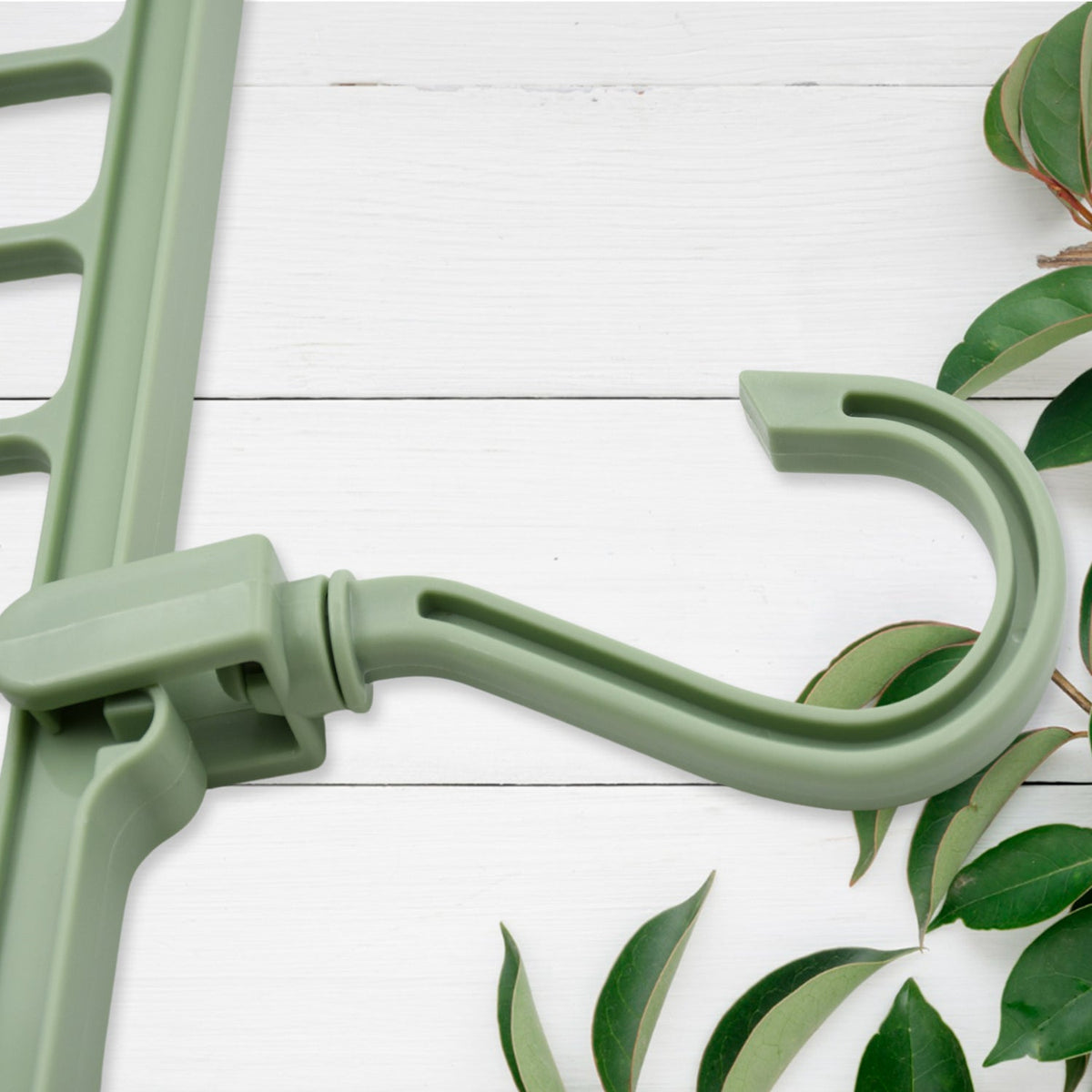 A close-up of the green plastic hook and part of the multi-hole hanger on a white wooden surface with leaves.