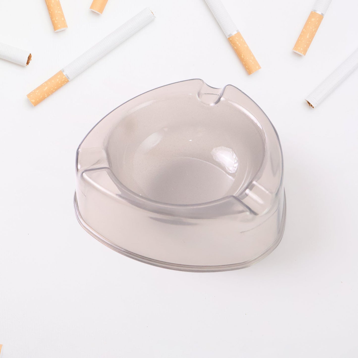 A purple transparent plastic ashtray is on a wooden table with pipes, a lighter, and pipe cleaning tools.