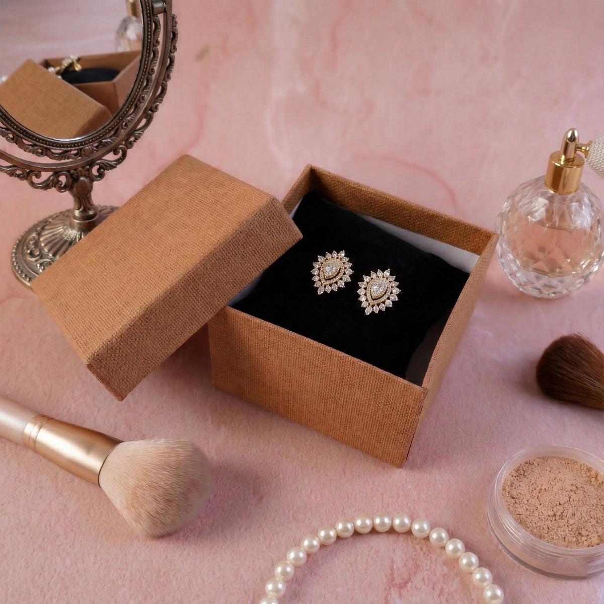 Brown textured gift box with sparkling teardrop earrings on a dark cushion, next to a vintage mirror.