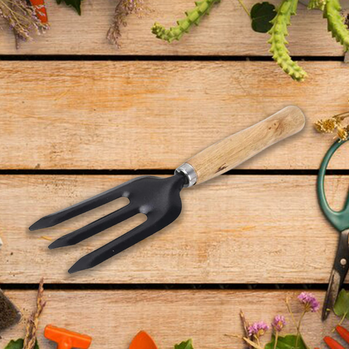 A black three-tine garden fork with a wooden handle is positioned on a rustic wooden surface with various gardening items.