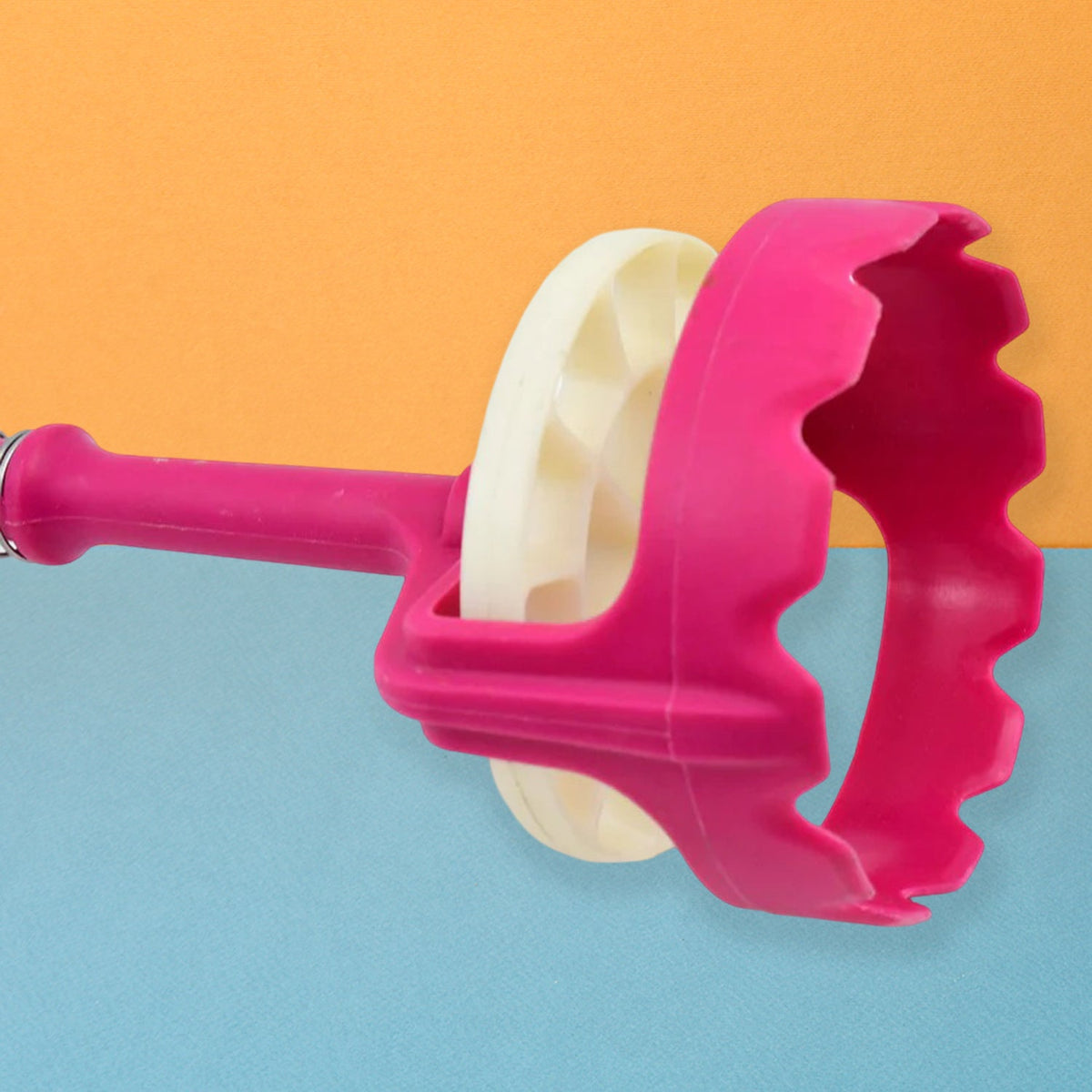 Close-up of the pink and white mashing head of the tool against a two-toned orange and blue background.