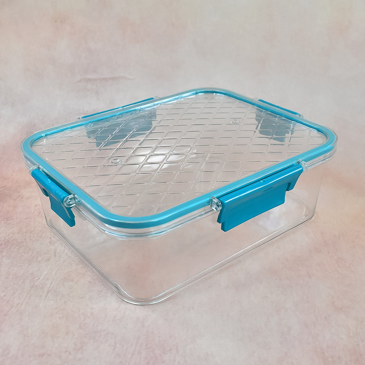 A single clear rectangular food container with a teal locking lid is shown on a light brown textured surface.