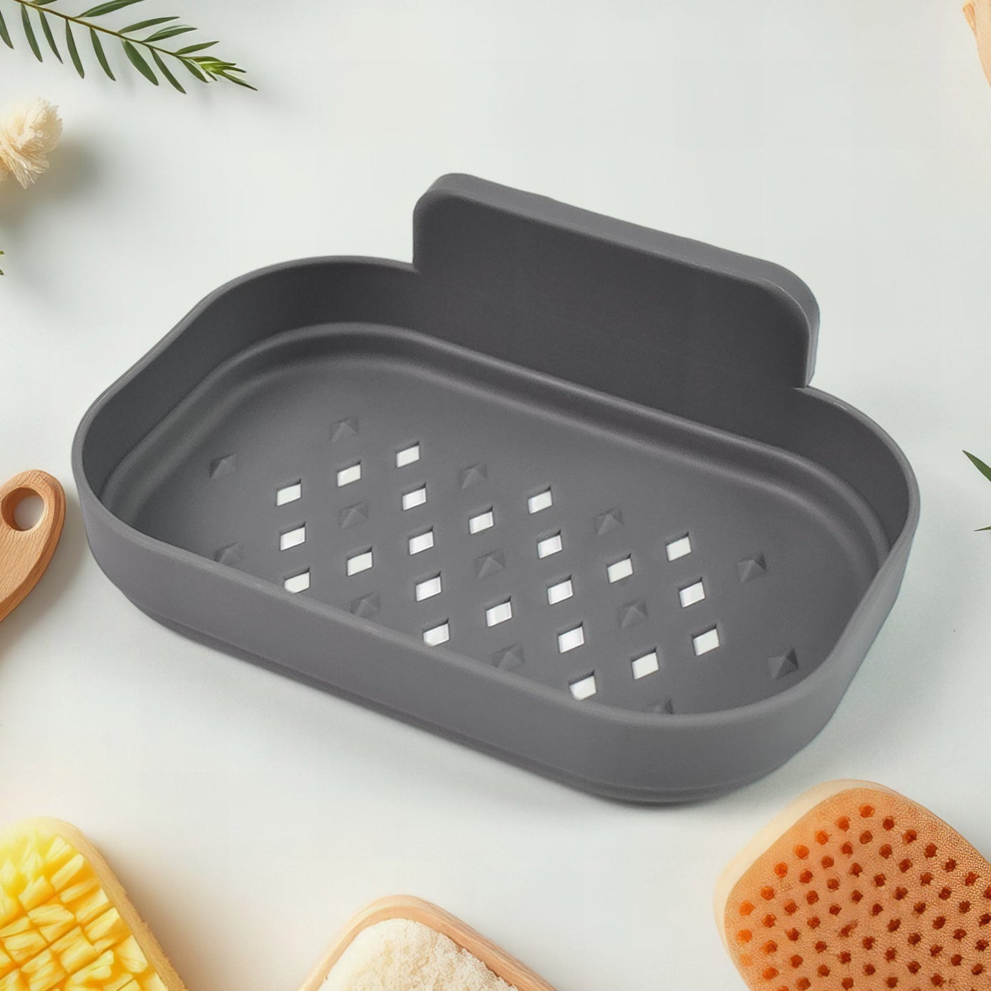 A gray self-adhesive soap dish with drainage holes is on a white surface surrounded by bath accessories.