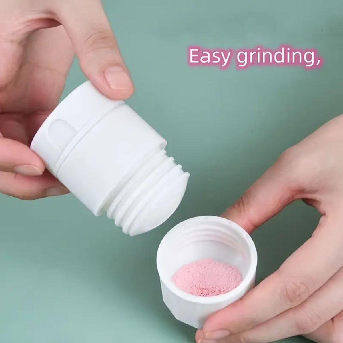 Hands holding a white pill grinder with pink crushed powder in the bottom section.