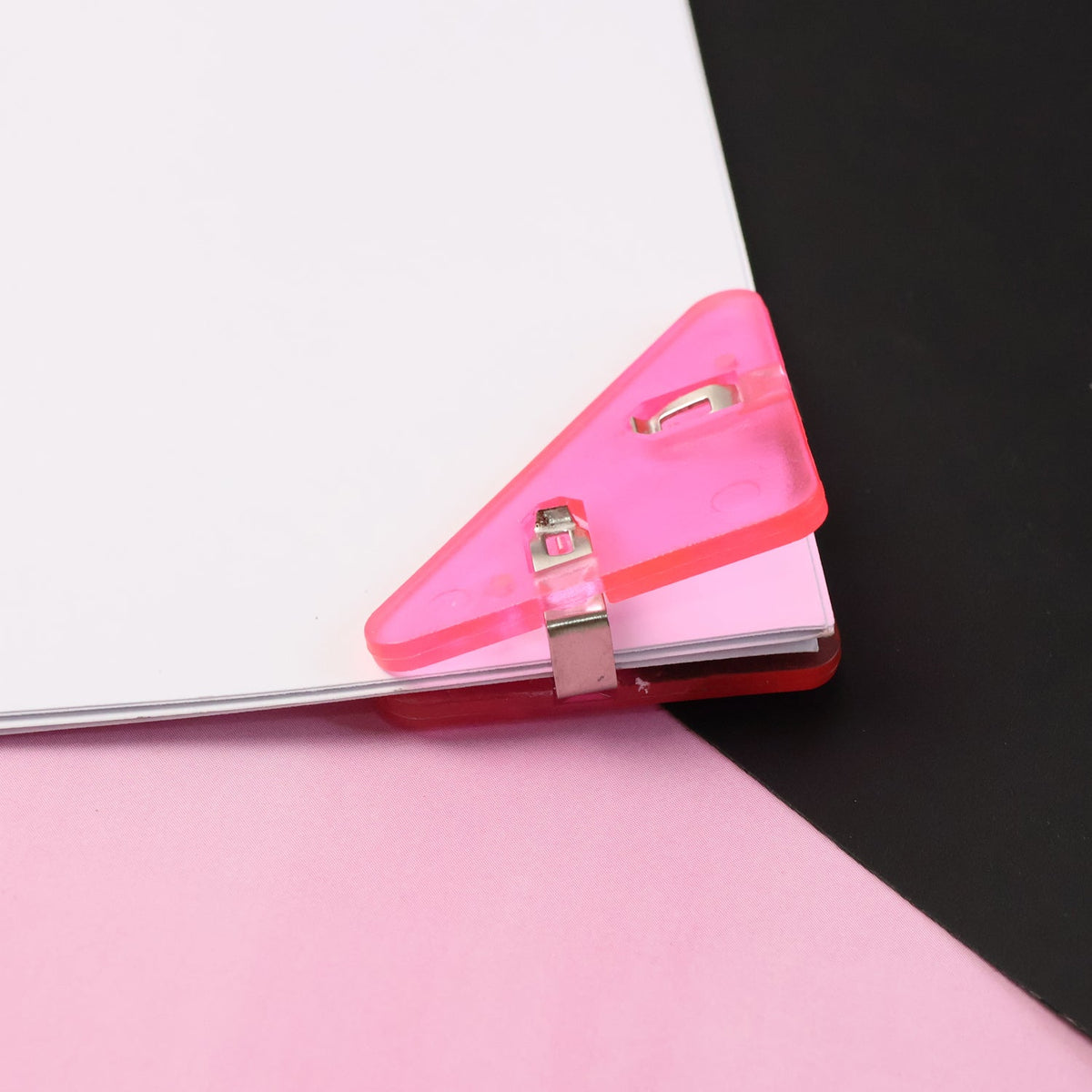 A pink plastic triangle corner clip securing papers on a pink and black background.