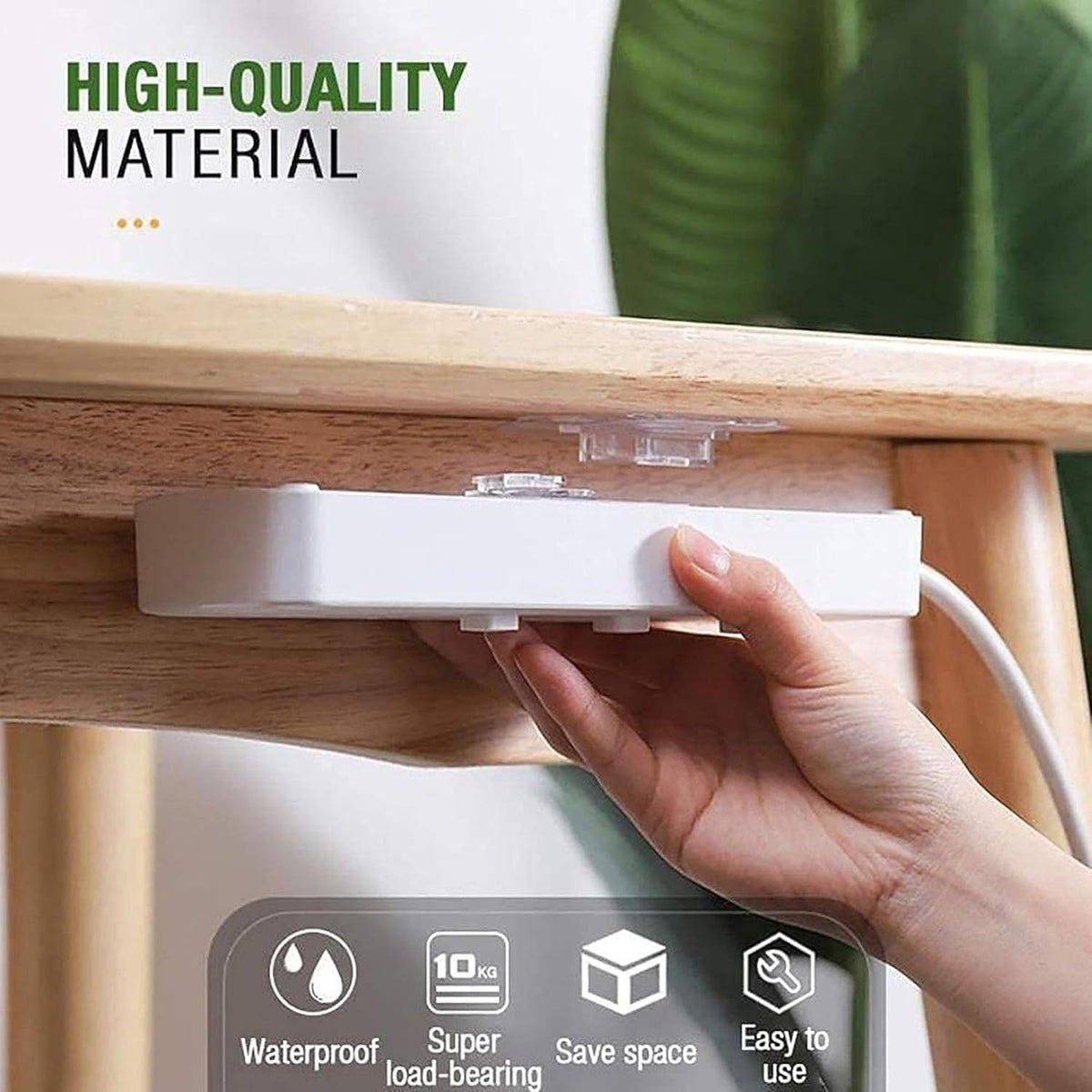 A hand attaches a white power strip to the underside of a wooden table using a clear adhesive hanger.