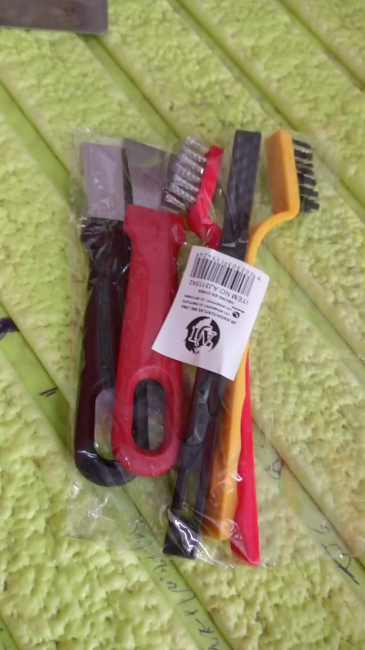 The five-piece cleaning set is packaged in a clear plastic bag with a white product tag, resting on a textured green surface.