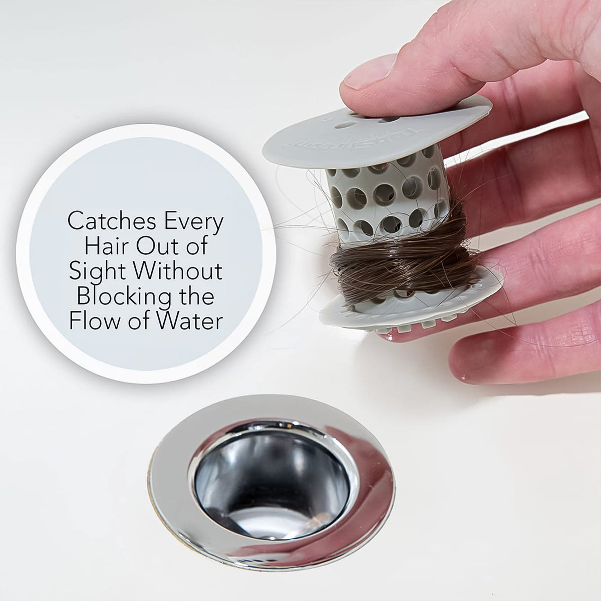 A hand holds the white silicone drain hair catcher with brown hair wrapped around it, next to a clean chrome drain, with