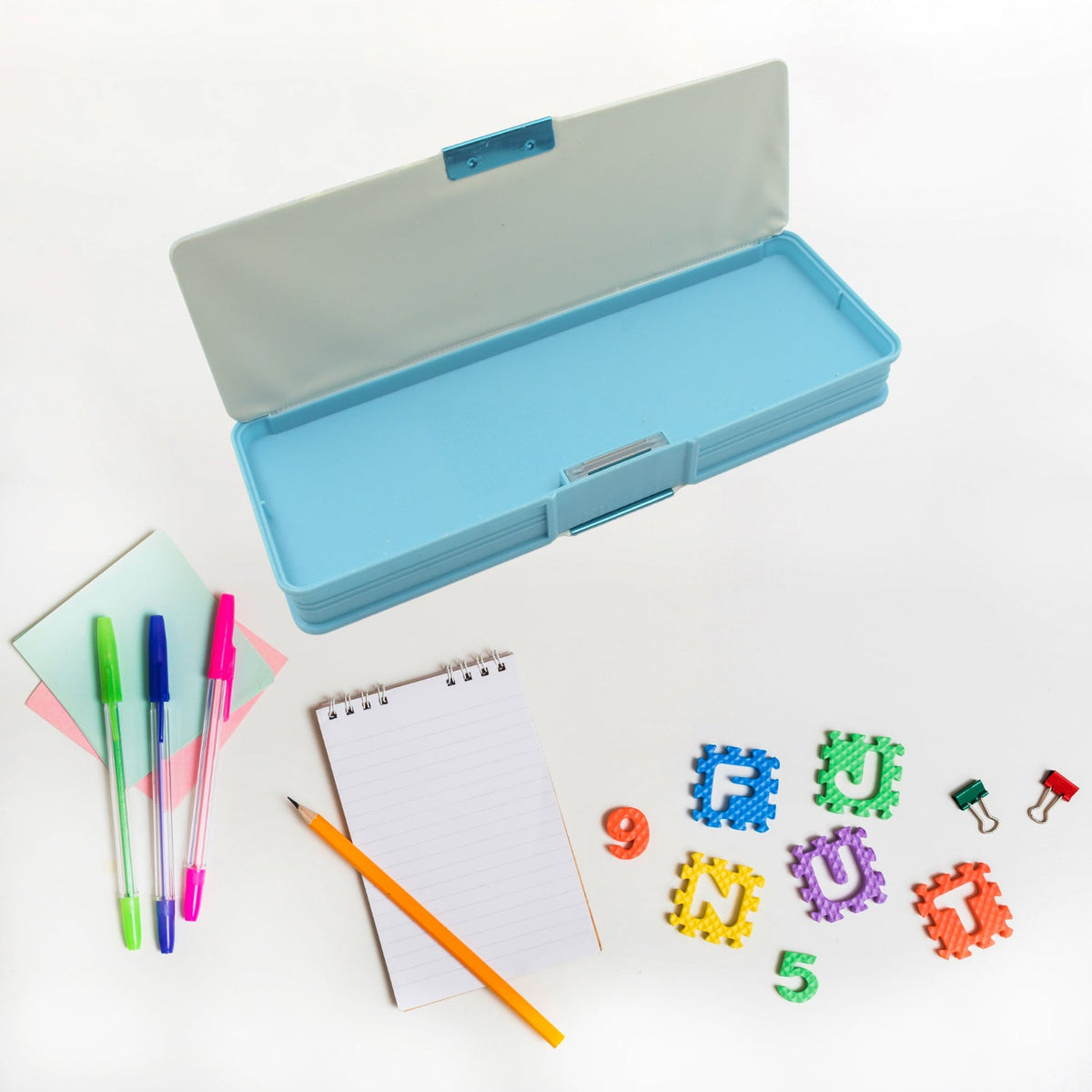 An open blue pencil case is surrounded by colorful pens, a small notebook, a pencil, and foam letter and number shapes.