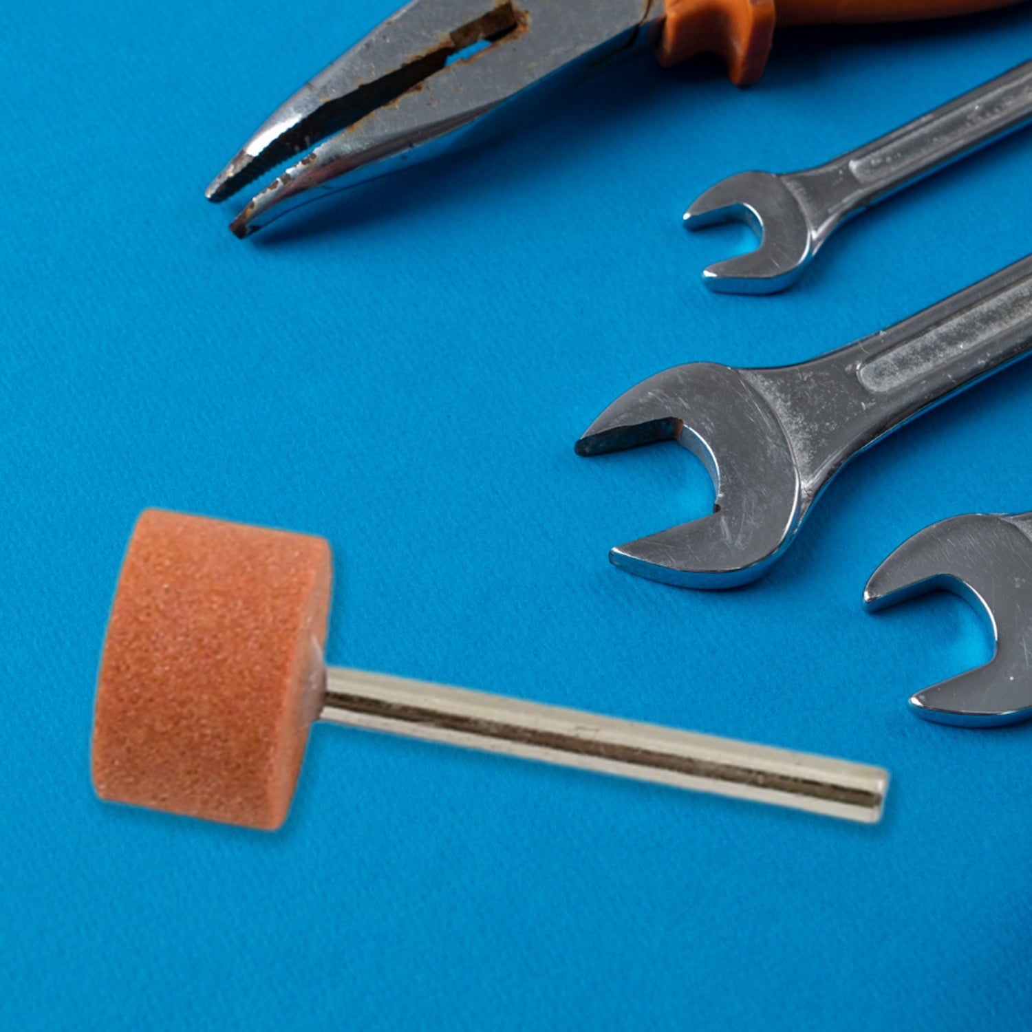 A single cylindrical abrasive grinding wheel on a blue surface surrounded by metal wrenches and pliers.