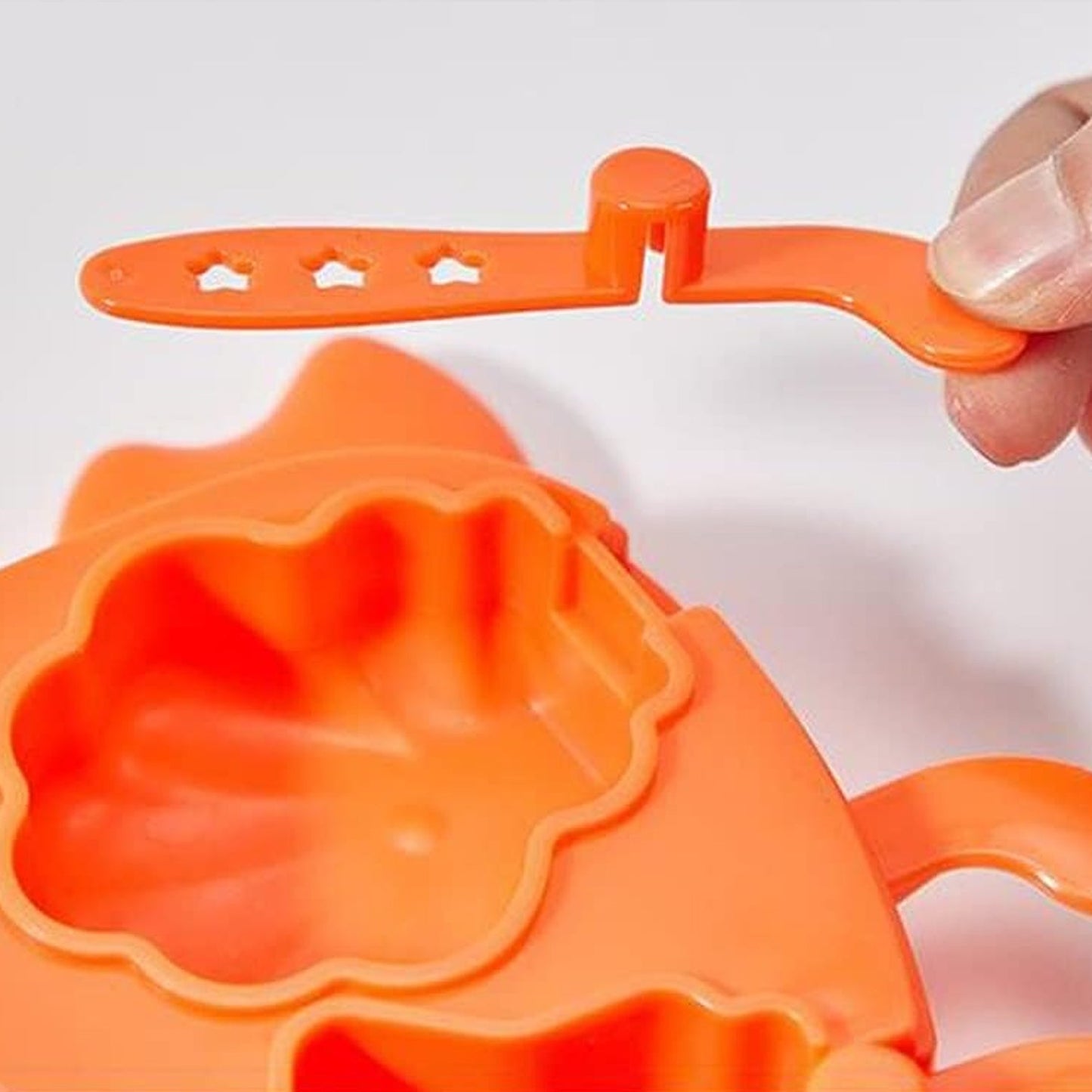 A hand holding an orange popsicle stick with star cutouts, above the open crab ice mold.