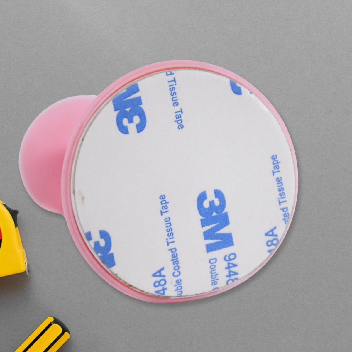 The adhesive backing of a pink silicone door stopper, showing a round 3M double-sided tissue tape sticker.