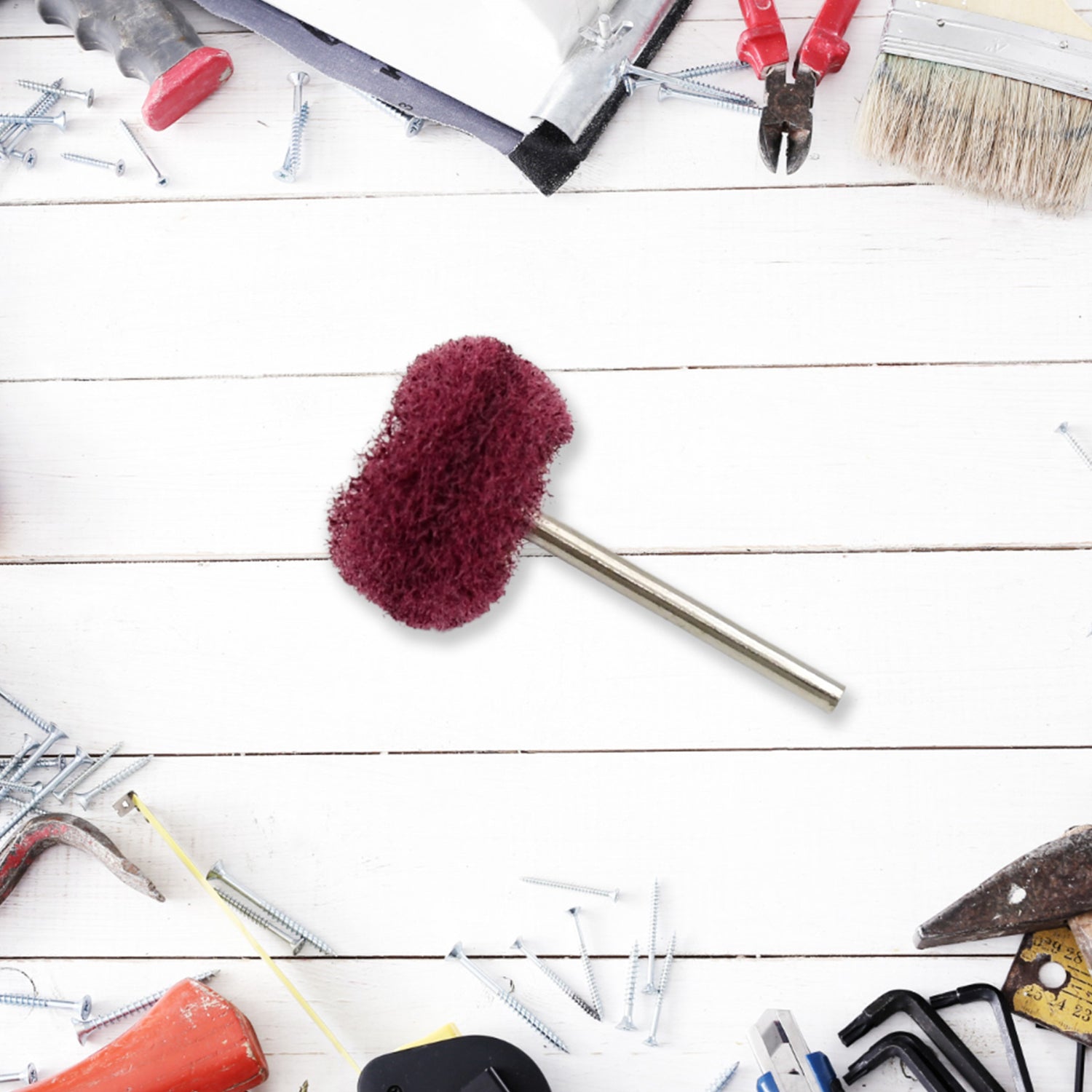 A single maroon buffing wheel centered on a white wooden surface with scattered tools and screws.