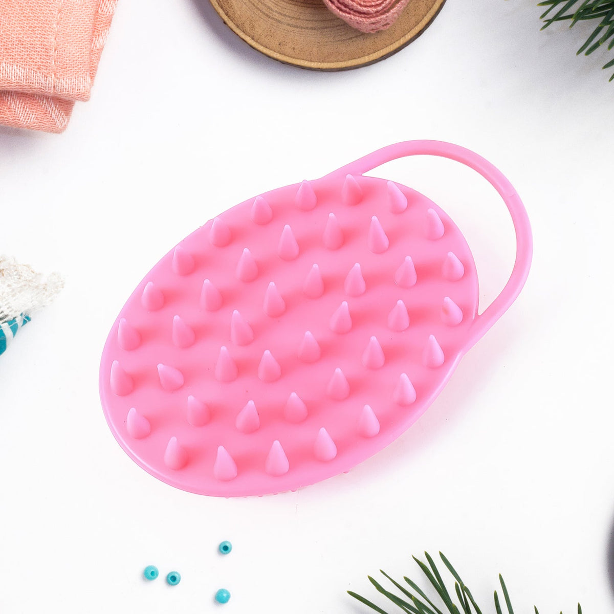 A pink silicone body brush with spiky bristles on one side and softer bristles on the other, is displayed on a white surface