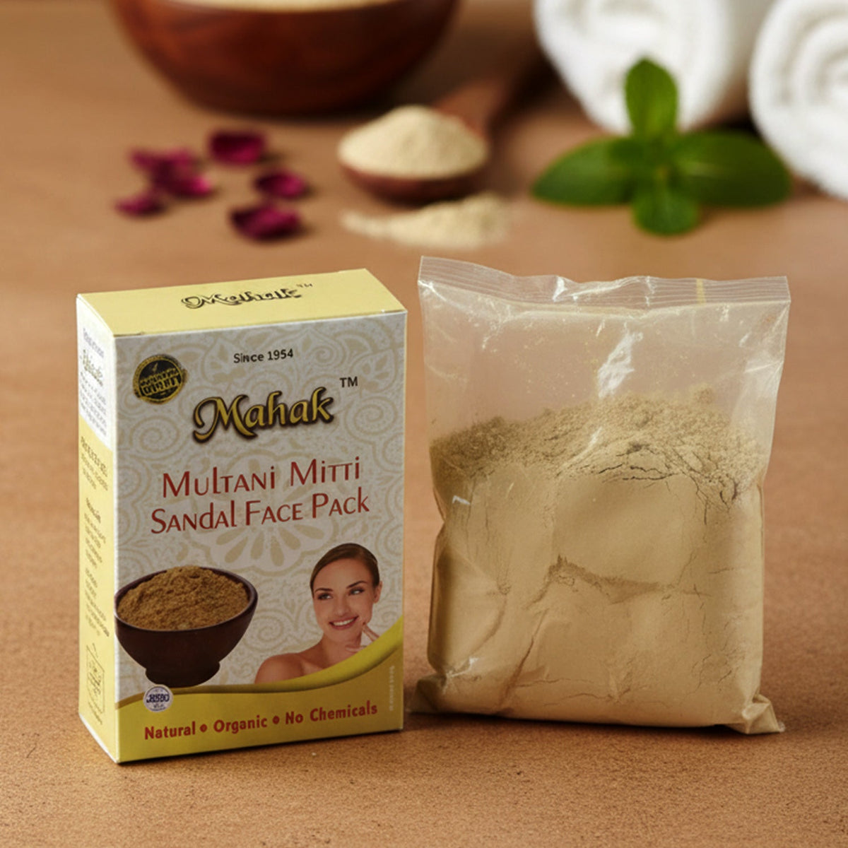 Mahak Multani Mitti Sandal Face Pack box and a clear bag of powder, with two white rolled towels and rose petals in the