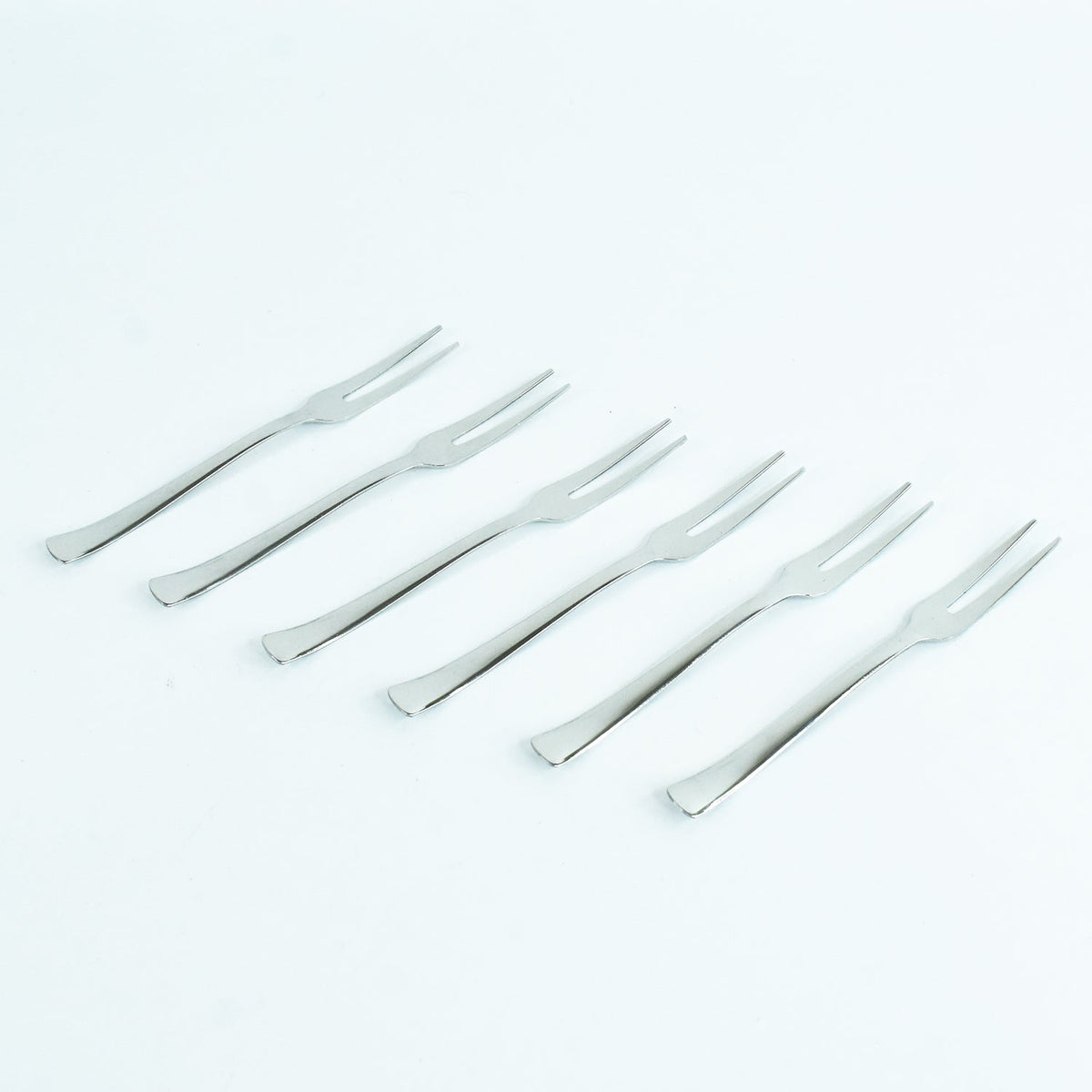 Six silver stainless steel fruit forks with two tines each, arranged diagonally on a plain white background.