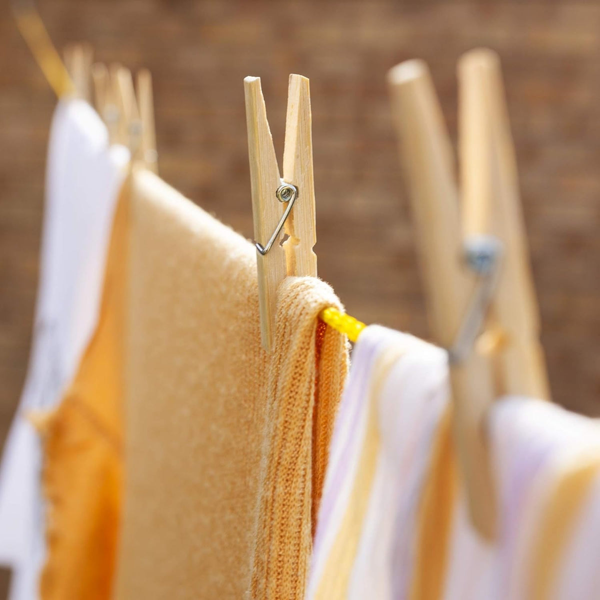 Three bamboo clothes pegs holding a yellow sweater and white striped shirt on a yellow clothesline.