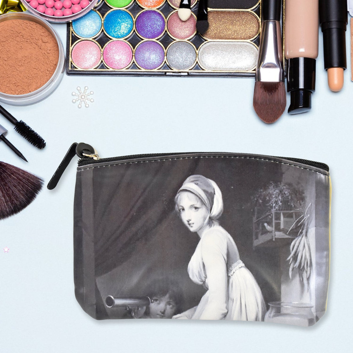 Black cosmetic bag with a classical portrait, on a light blue surface surrounded by makeup items.