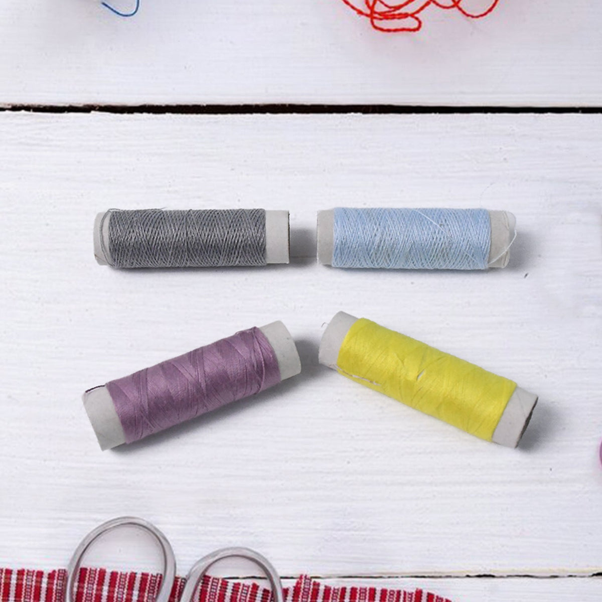 Four spools of thread in grey, light blue, purple, and yellow arranged on a white wooden surface.