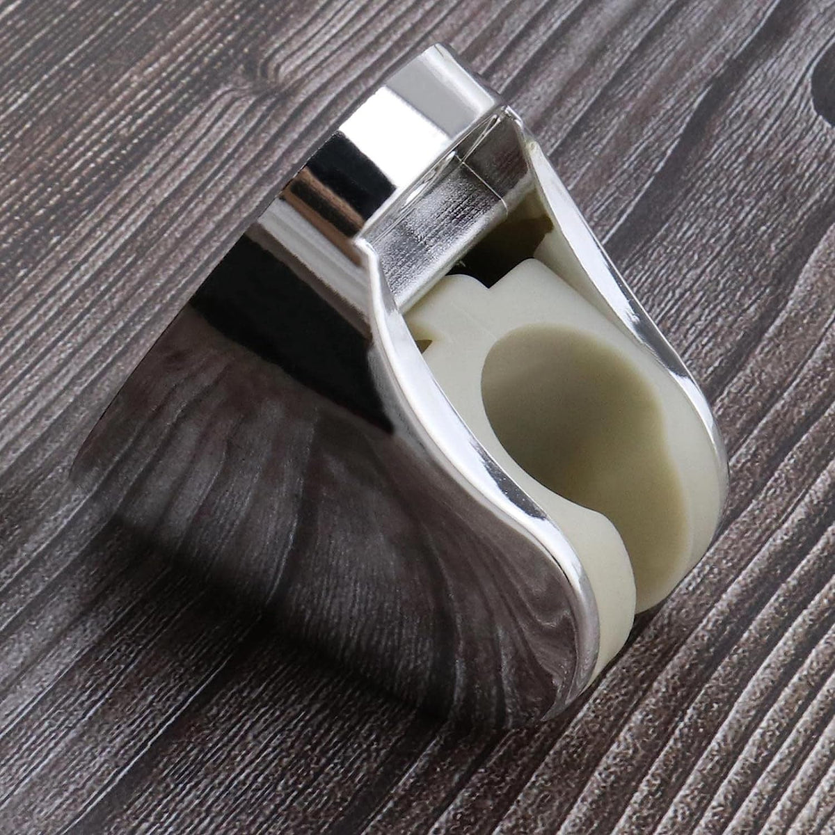 A chrome shower head holder with a beige interior is angled on a dark brown wooden surface, highlighting its reflective