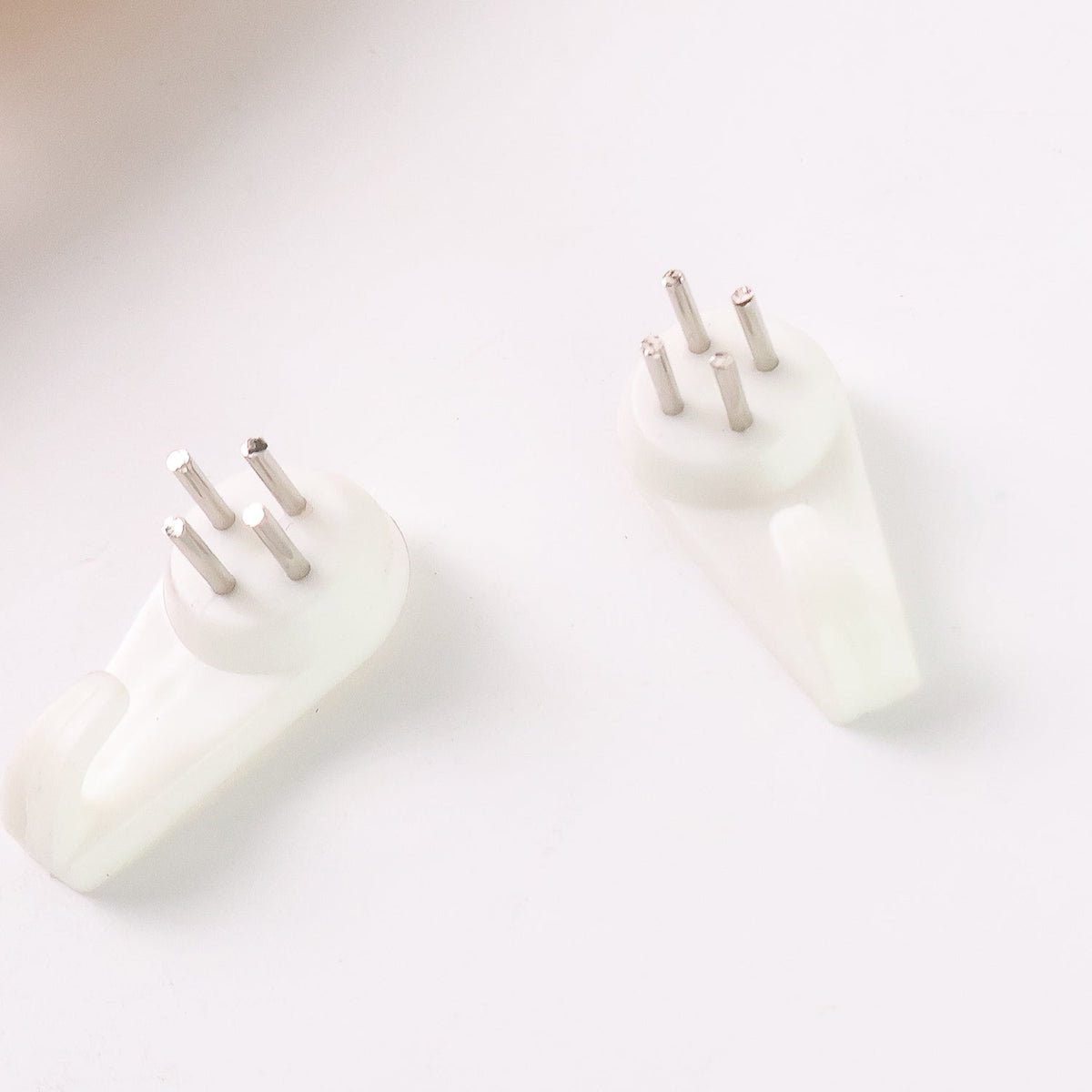 Two white plastic wall hooks with three metal pins each are shown on a white surface.